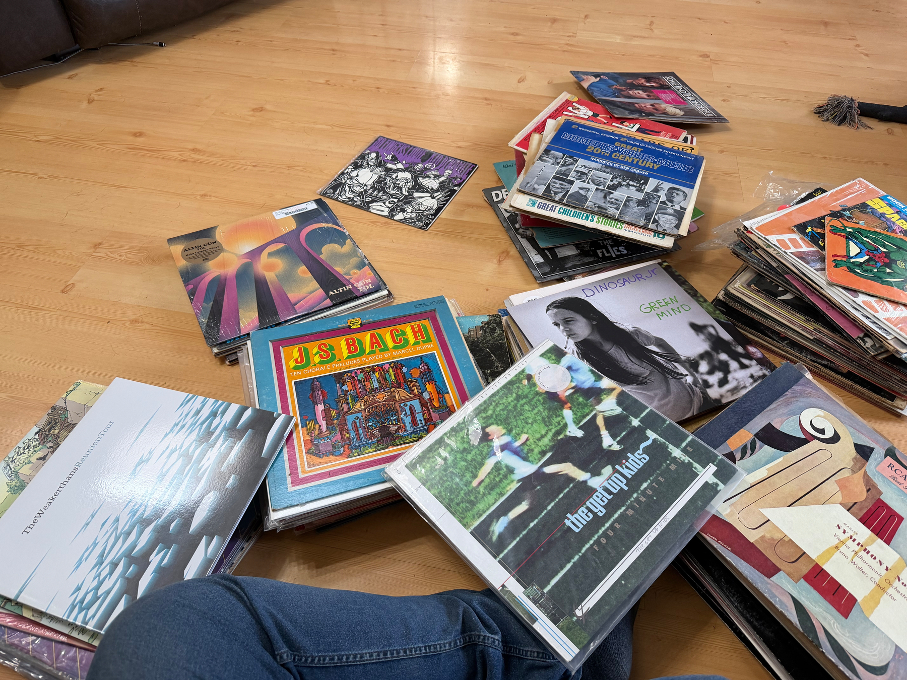 My legs surrounded by various vinyl record covers scattered on a wooden floor.
