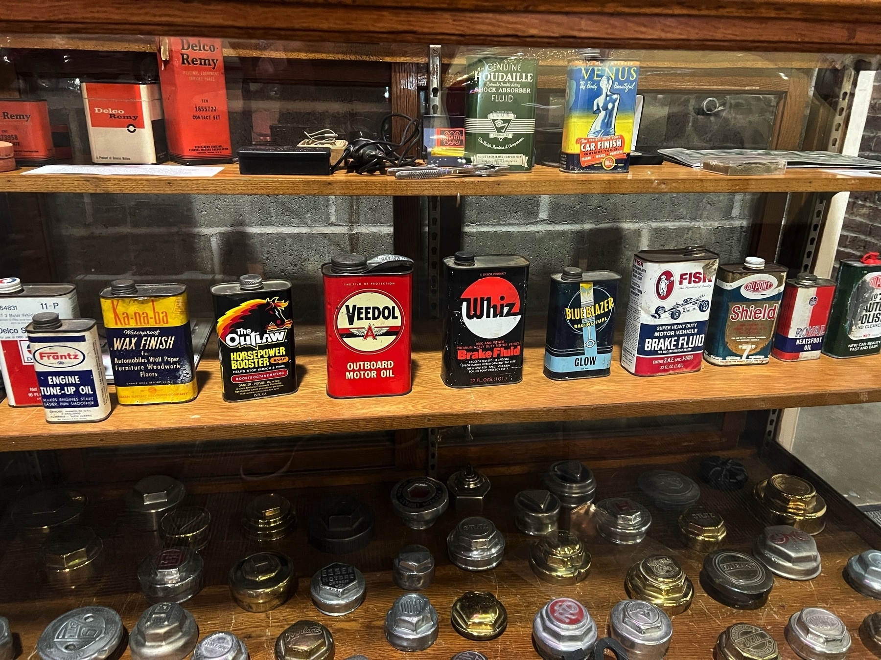A display cabinet contains vintage oil cans and various metal caps on shelves.