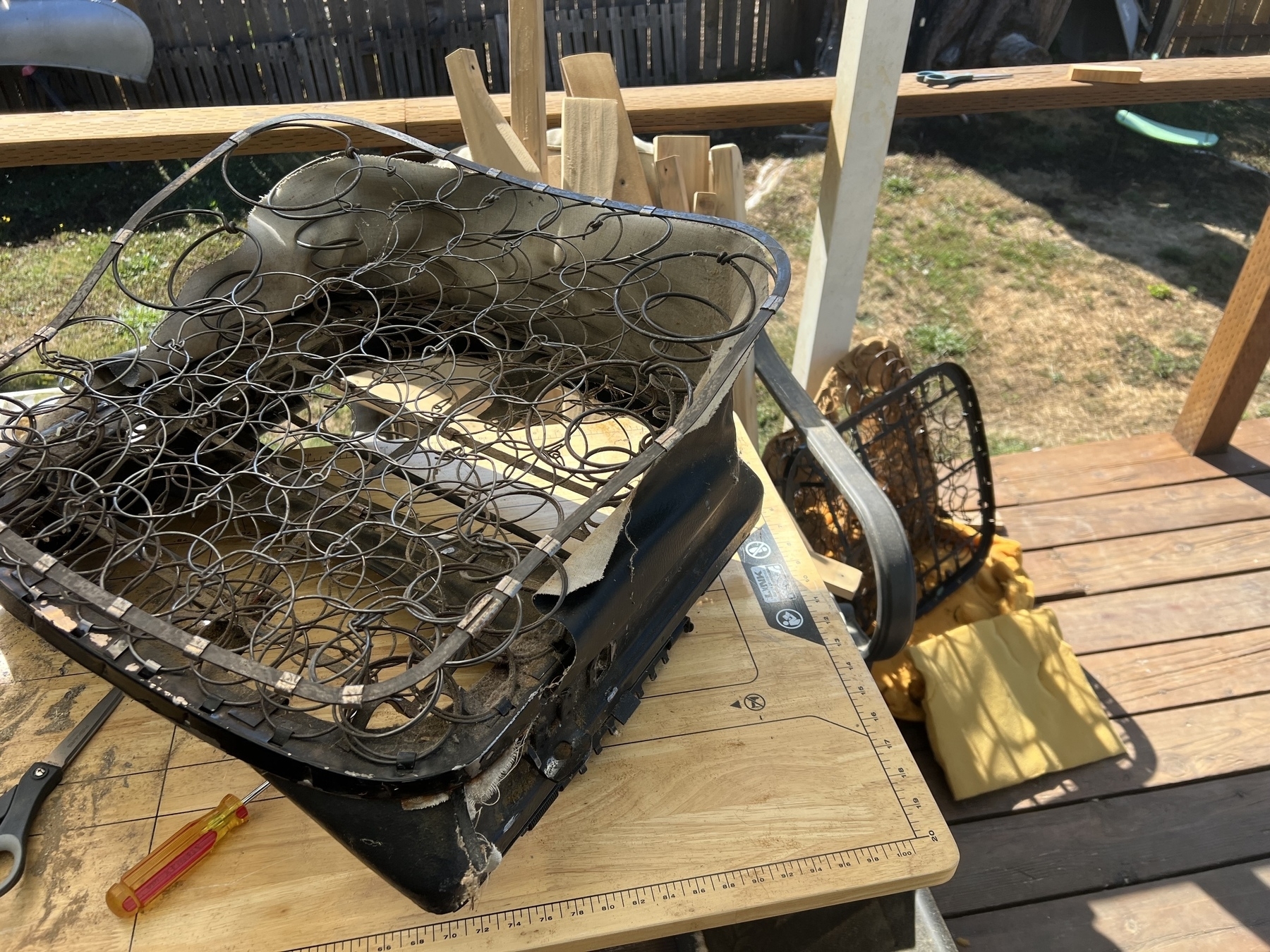 A disassembled and exposed 72 squareback chair frame with visible springs is placed on a wooden worktable outdoors, surrounded by tools and scraps.