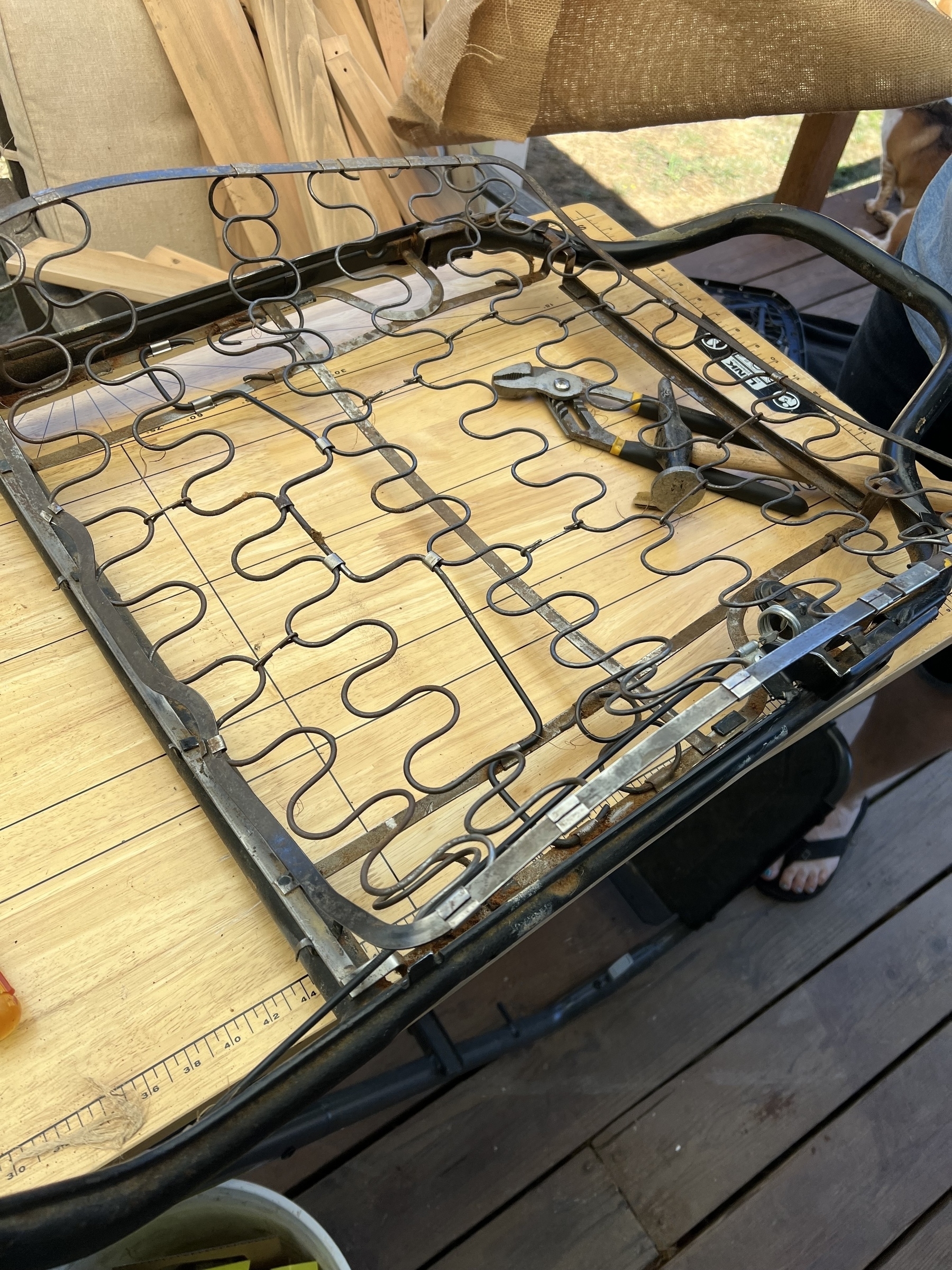 A upper 69 chair frame with springs is placed on a wooden table along with some tools.
