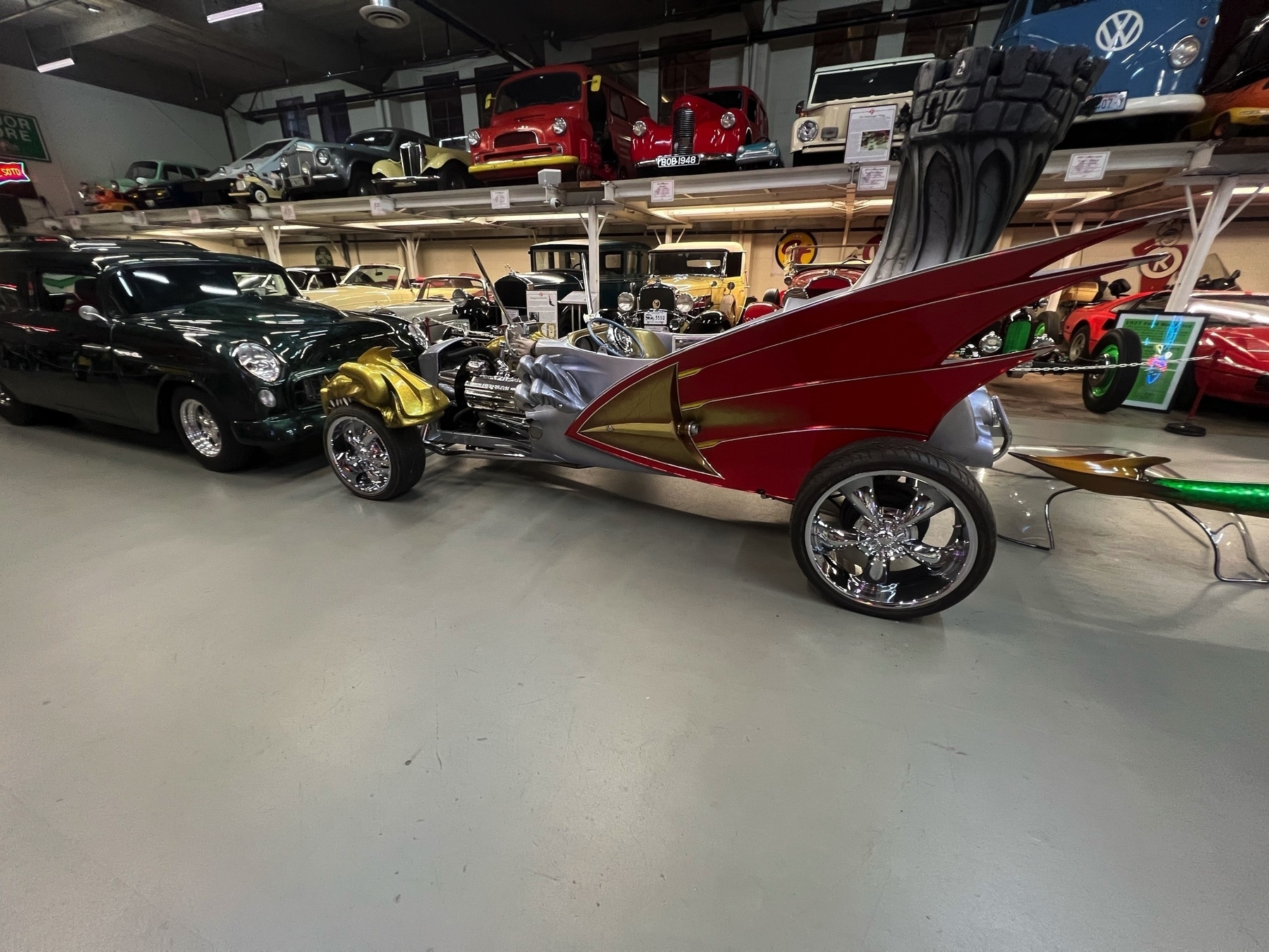 A collection of unique and vintage cars is displayed in a showroom, featuring a vehicle with a distinctive red and gold wing-like design.