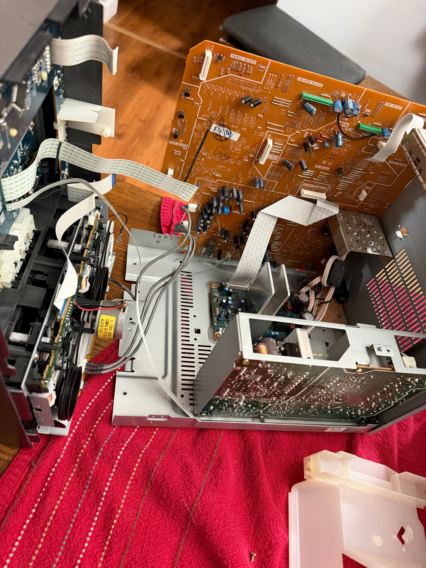 A dismantled electronic device with exposed circuit boards, wires, and components is spread out on a red surface.