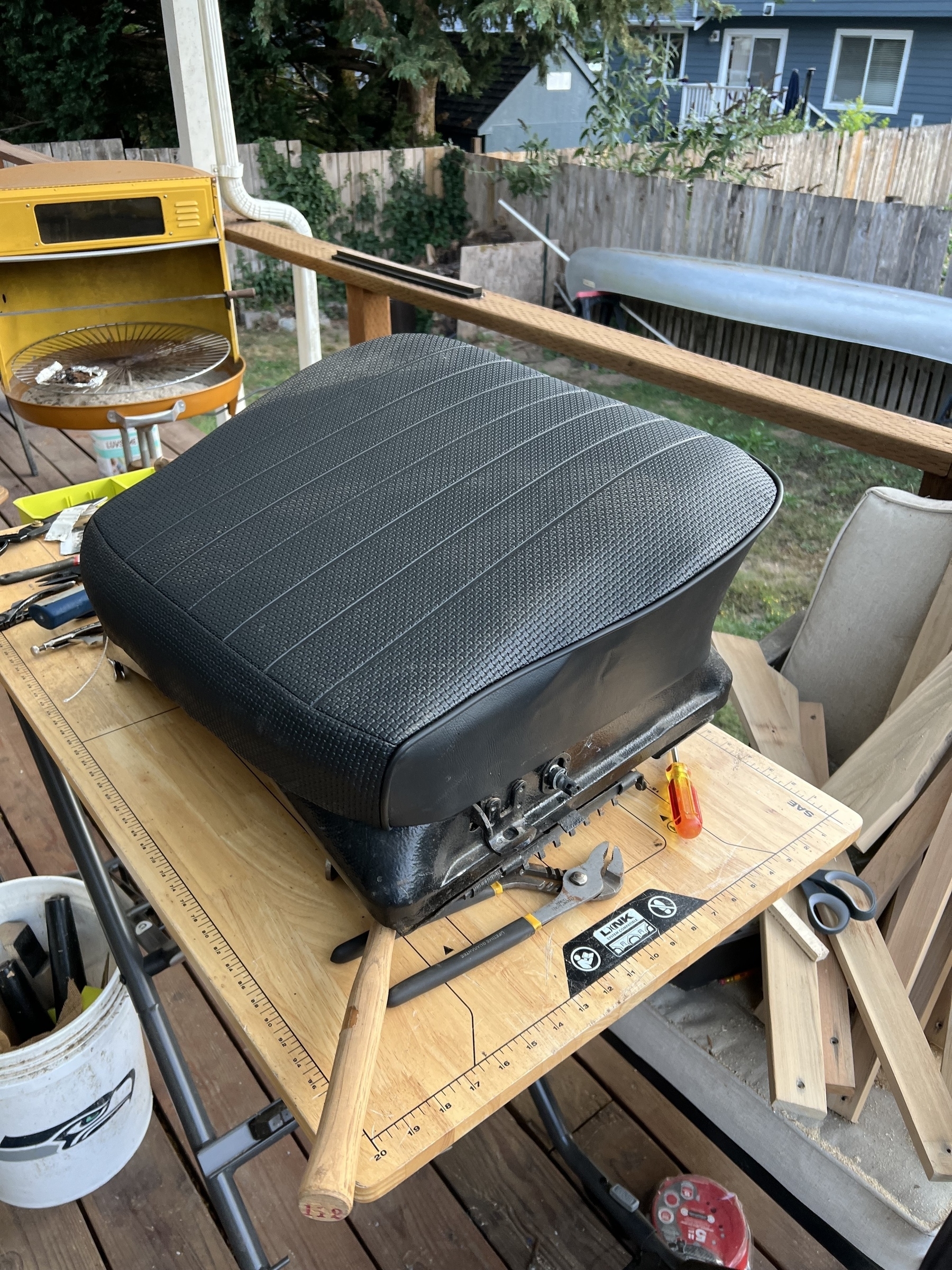 A finished 72 VW car seat is placed on a table surrounded by various tools and woodworking items on a porch.