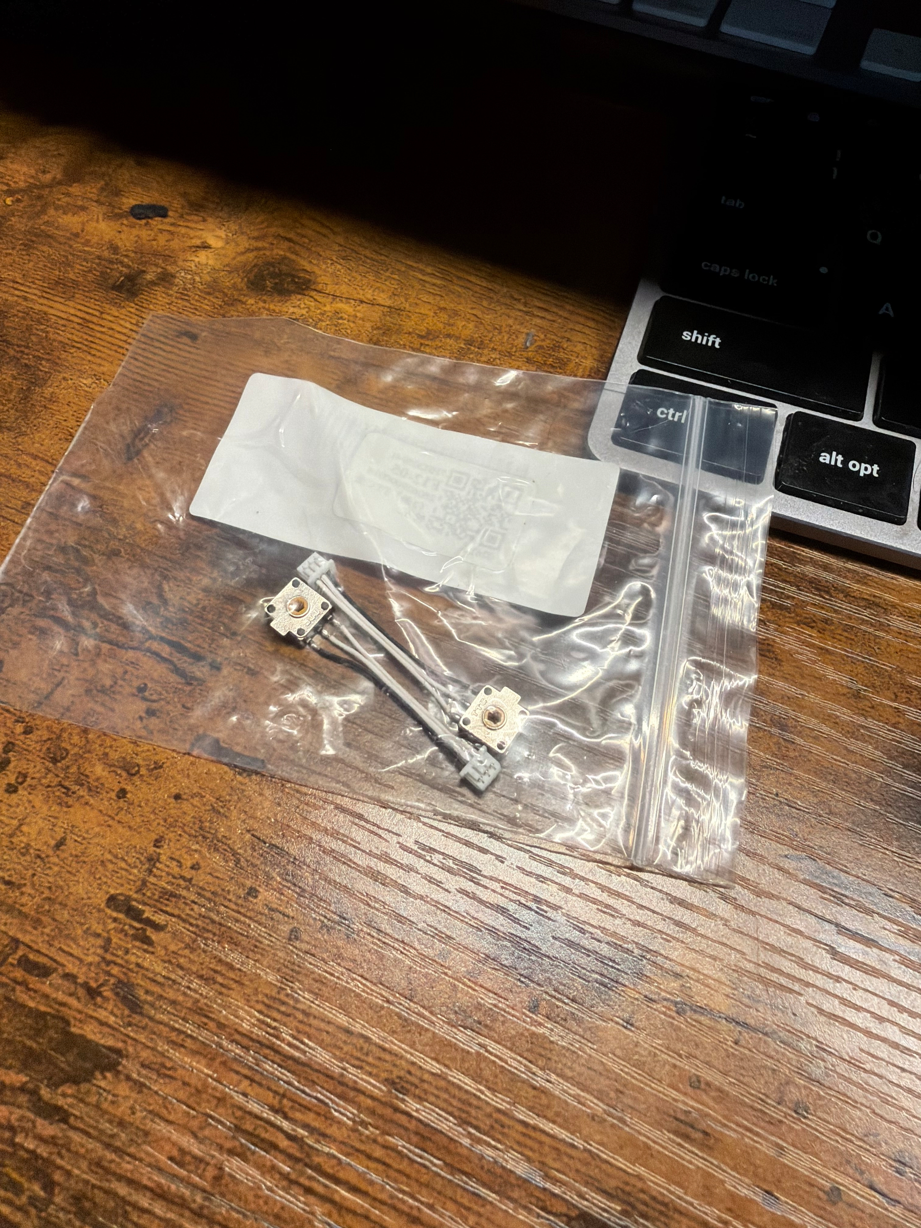 A small plastic bag containing mouse scroll wheel encoders components rests on a wooden surface beside a keyboard.