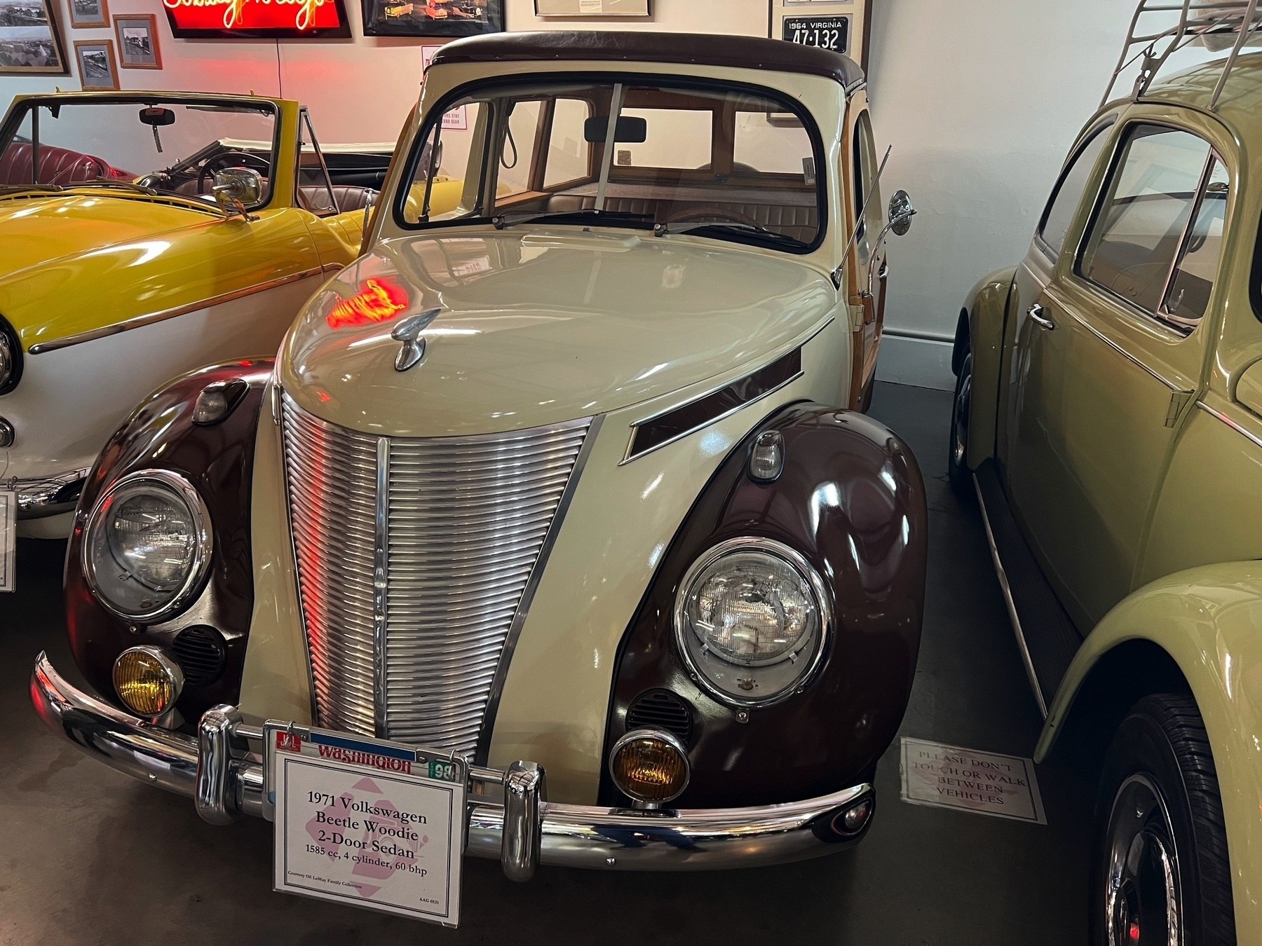 Someone made a vintage Volkswagen Beetle with a unique front grille look like a Morris Minor. Displayed between two other classic cars in a showroom setting.