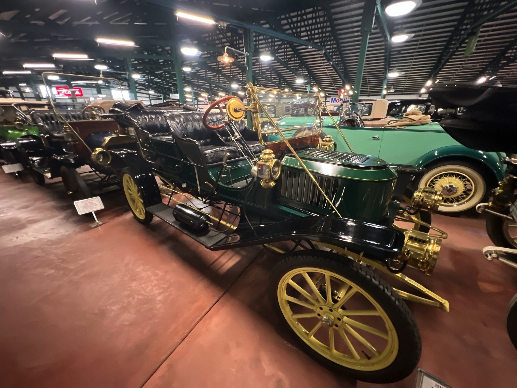 A vintage automobile with a brass radiator and leather seats is displayed in a museum setting.