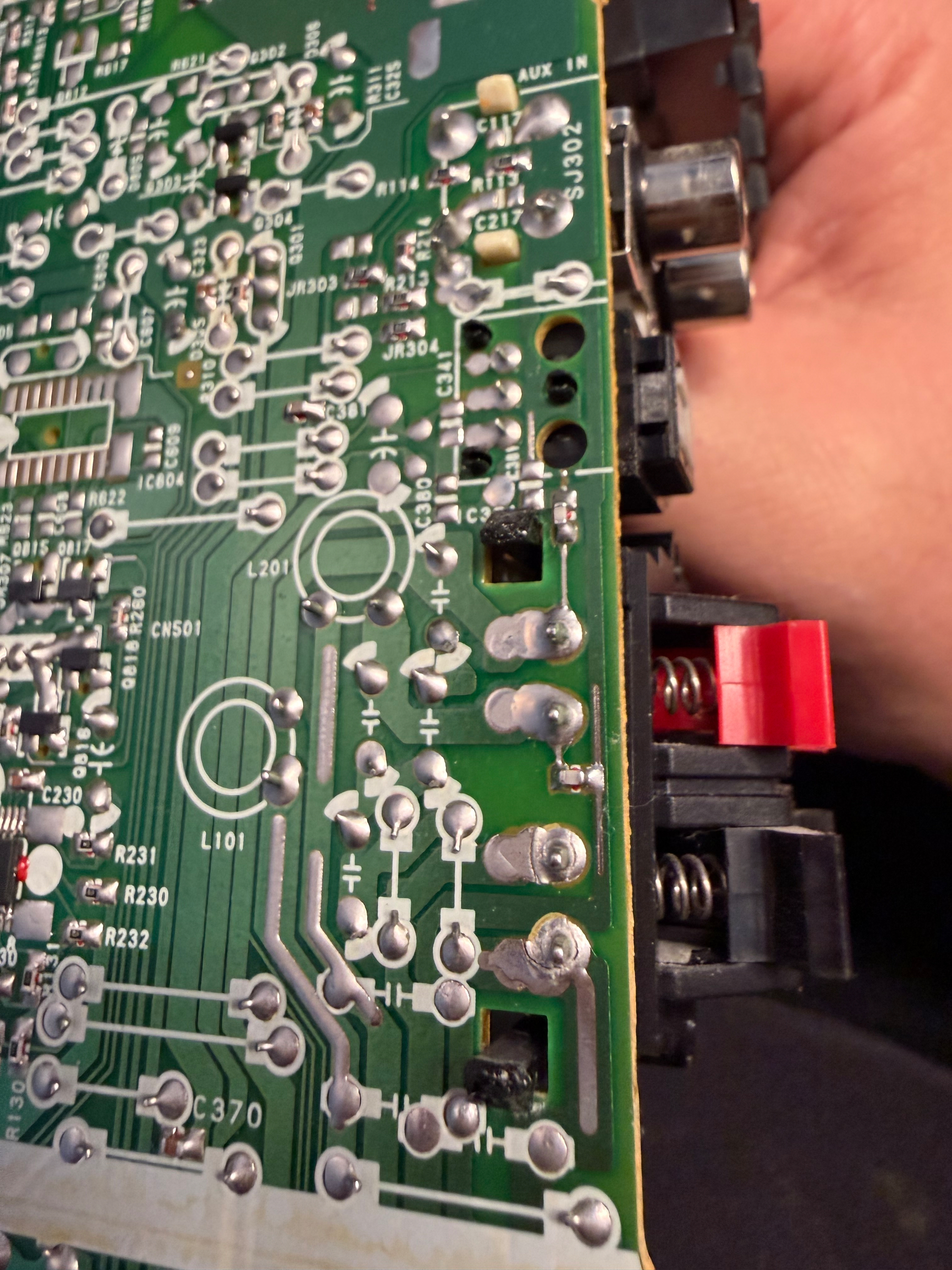 A close-up view of a green circuit board being held by a hand, featuring various electronic components and soldered connections.