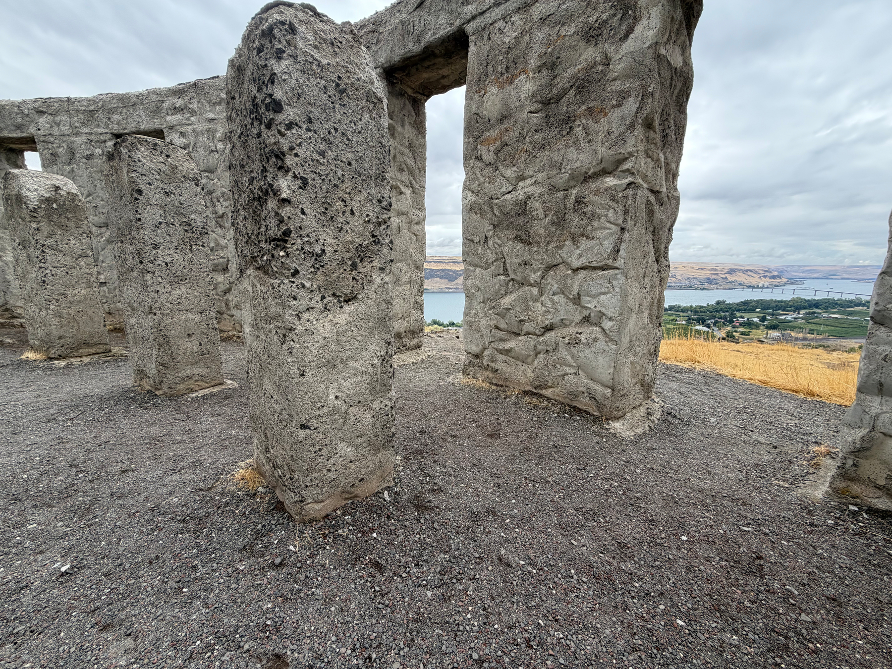 A portion of the full size concrete replica of Stonehenge stands on a hill with a view of the Columbia river and surrounding landscape in the background.