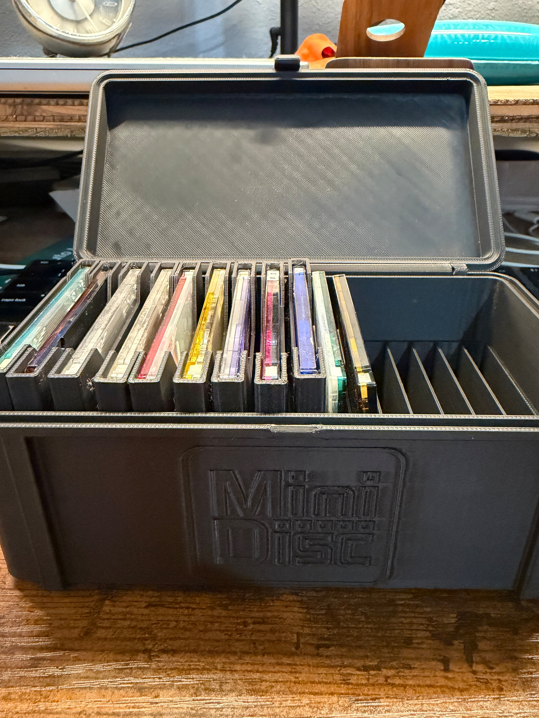 A black storage case labeled Mini Disc contains several MiniDisc cartridges organized in individual slots.