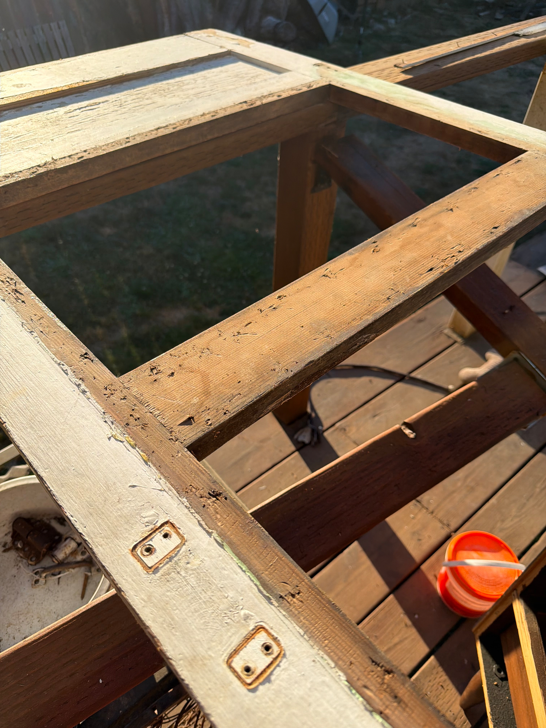 A weathered, partially disassembled wooden door frame lies on a wooden deck with a small orange container nearby.