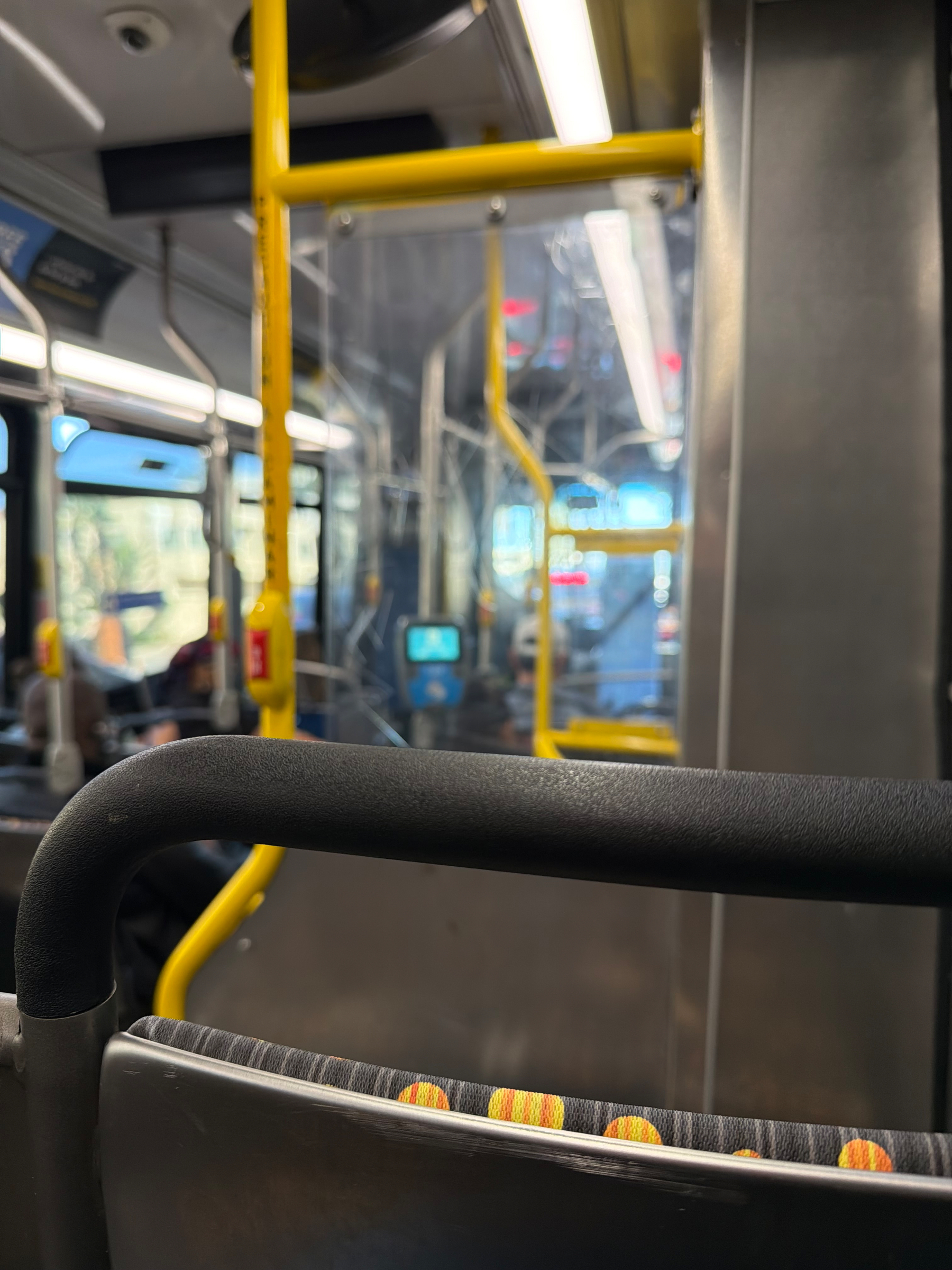 Inside a bus, the view shows seating, handrails, and reflections from the windows.