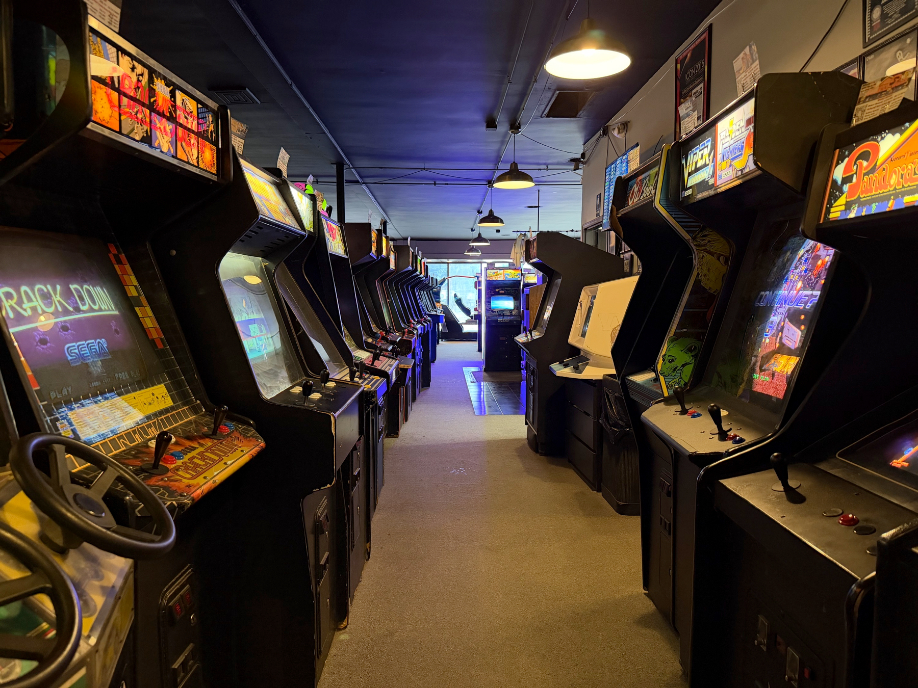 An arcade room is filled with rows of classic arcade game machines lining both sides of a central aisle.