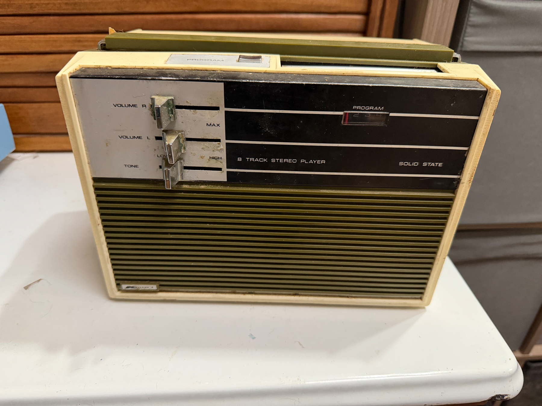 A vintage 8-track stereo player with volume and tone controls is resting on a table.