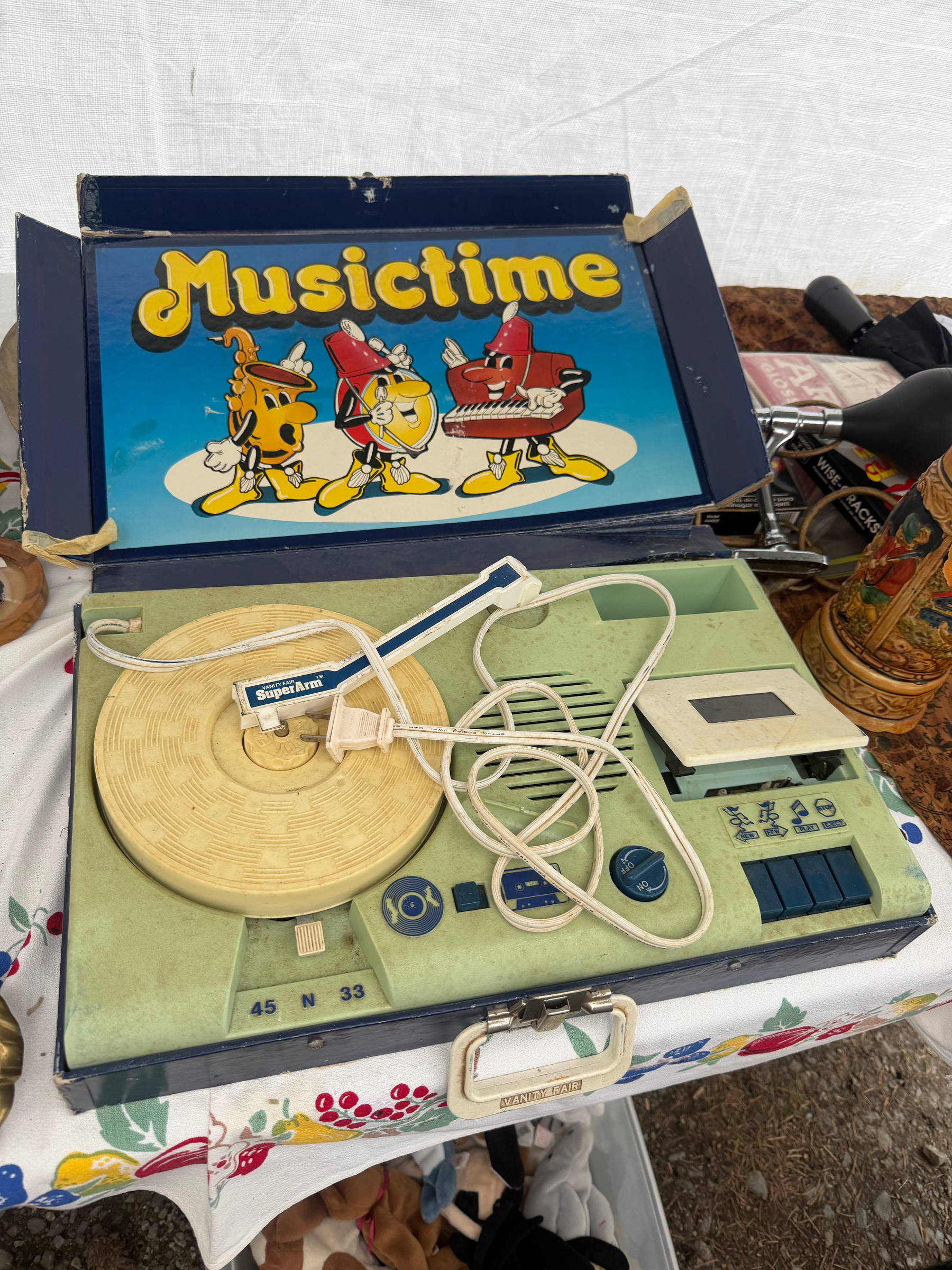 A vintage Musictime record player with cartoon characters on the cover is displayed on a table with a colorful tablecloth.