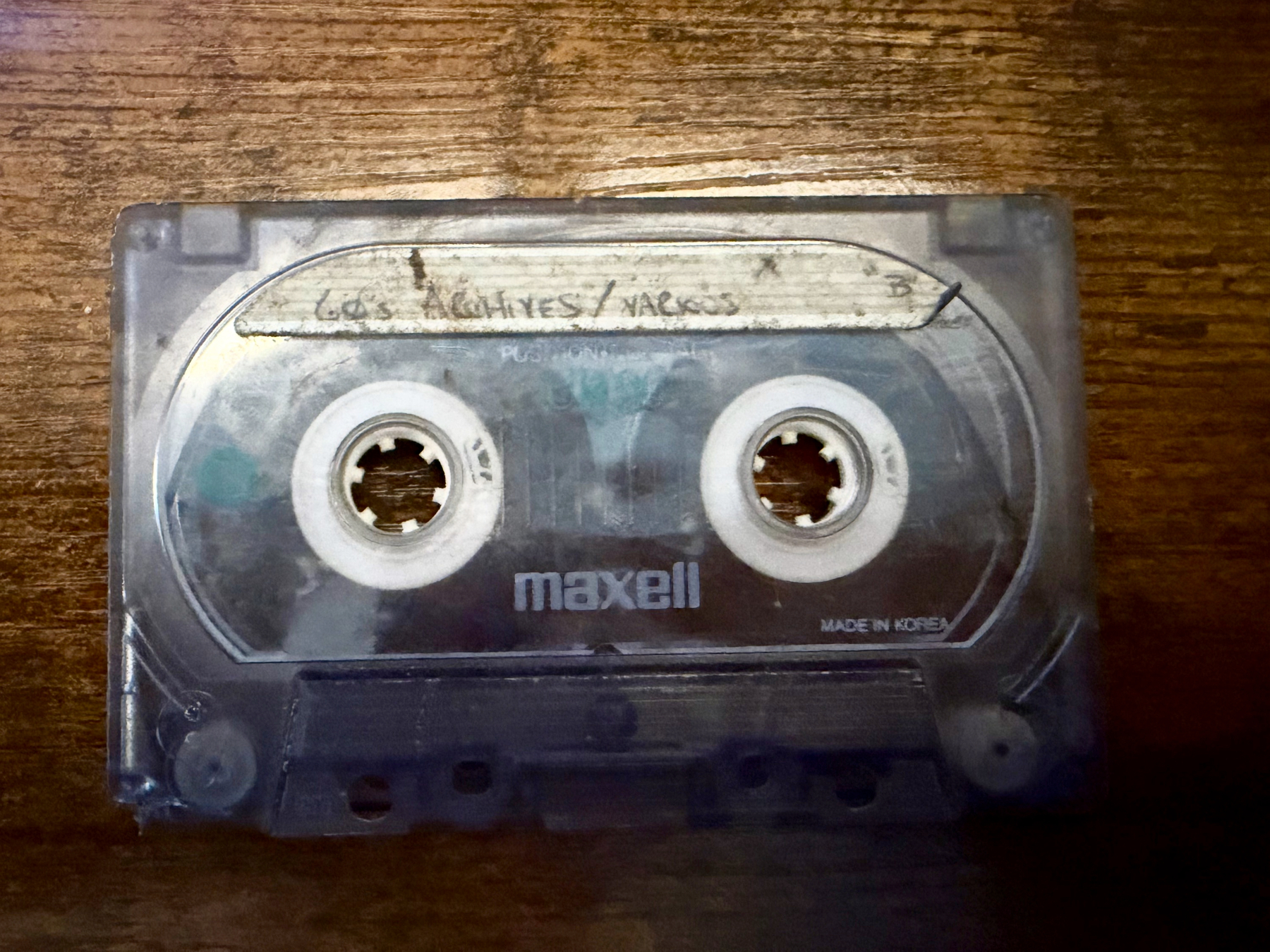 A clear Maxell audio cassette tape with handwritten labeling is placed on a wooden surface.