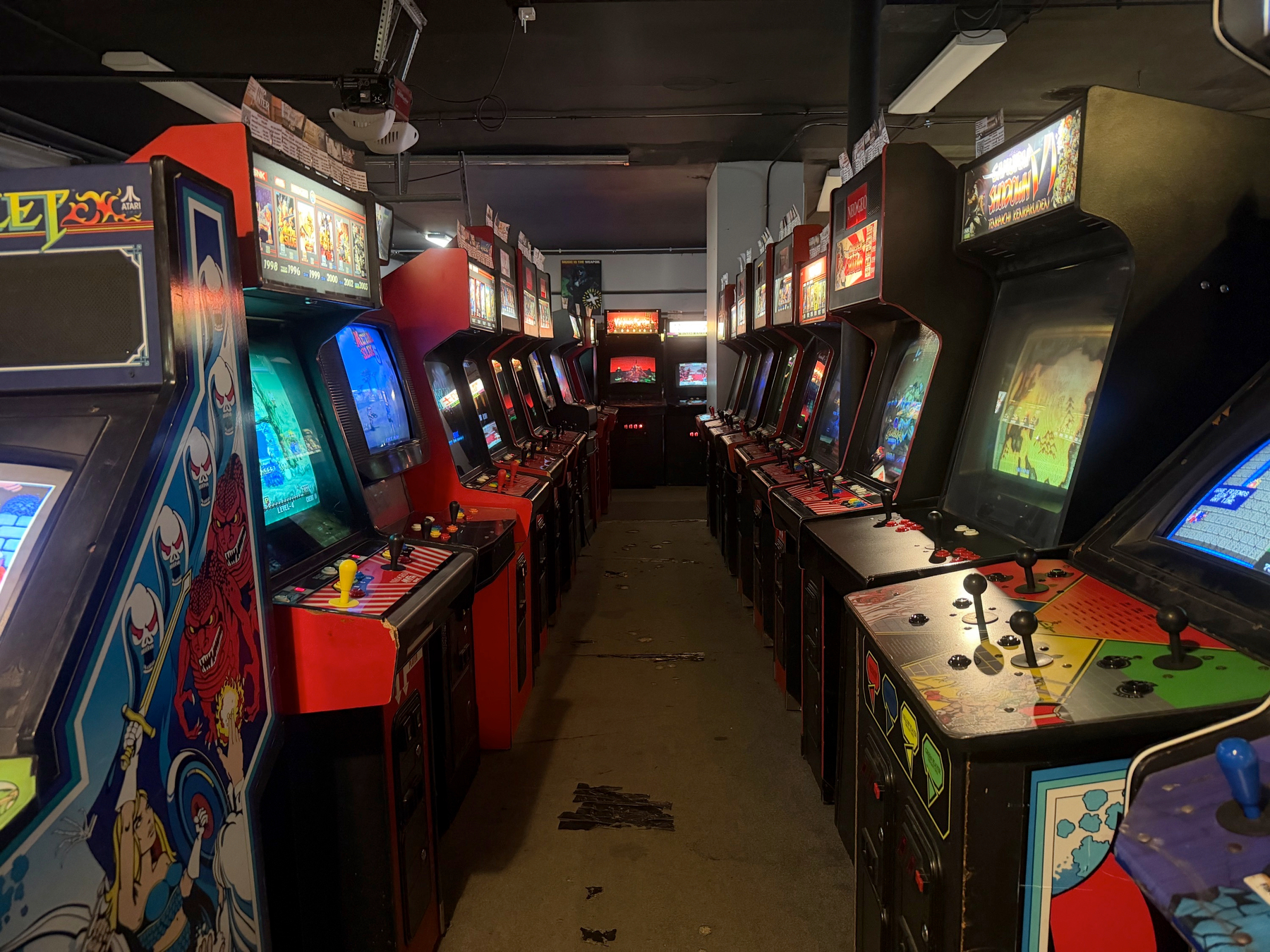A narrow arcade room filled with rows of vintage arcade game machines lining both sides.