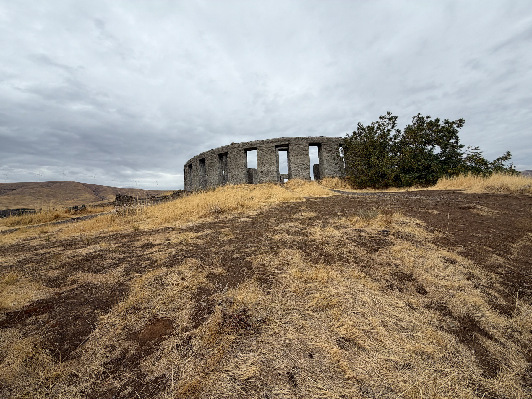 The Stonehenge memorial viewed from down the slope stands on a dry, grassy hill under a cloudy sky.