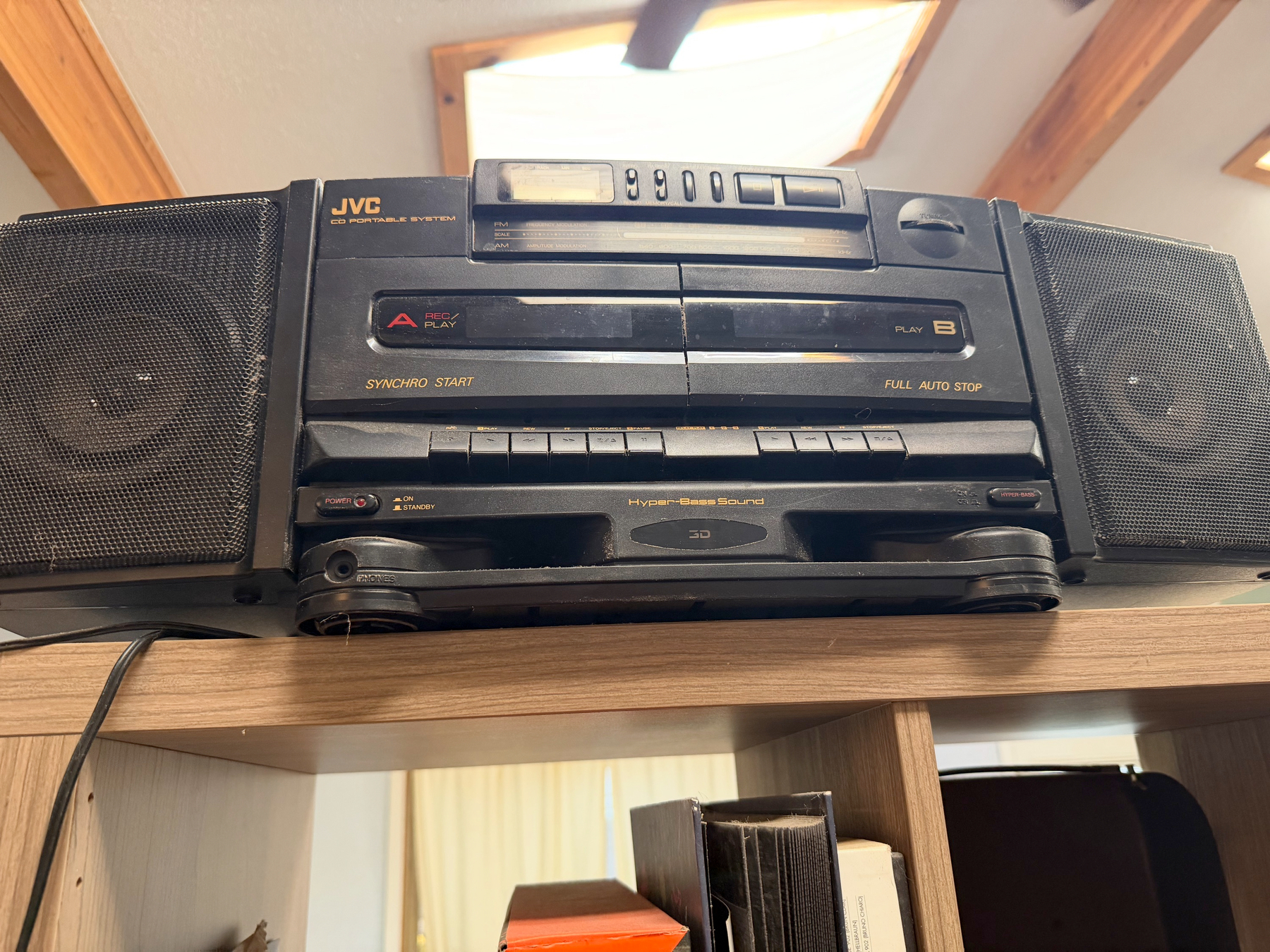 A JVC stereo system with dual cassette decks and two speakers is placed on a wooden shelf.