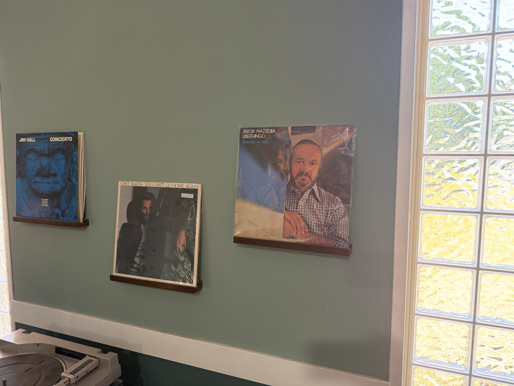 Three vinyl record albums are displayed on small wooden shelves mounted on a green wall above a turntable.