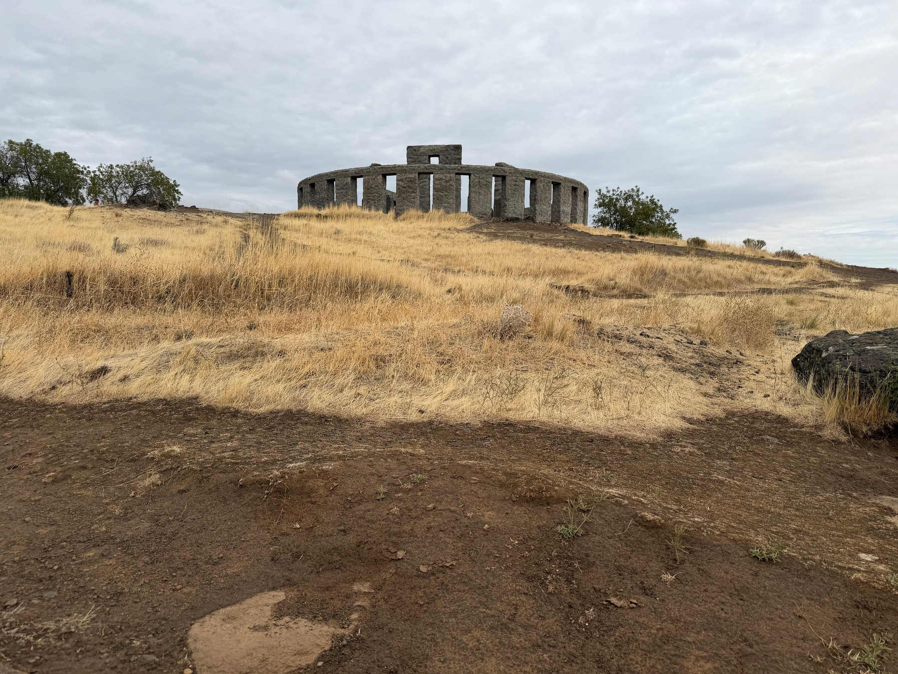 Stonehenge (replica) stands atop a grassy hill under a cloudy sky.