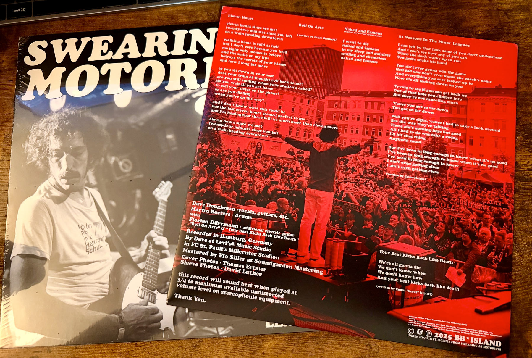 A black-and-white photo of a guitarist performing live is featured on the cover of an album titled Swearin Motor, alongside a red insert with lyrics and a live concert photo of a crowd and a person addressing them.