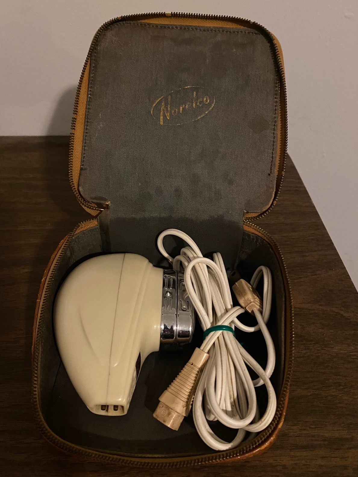 A vintage electric razor with a coiled cord is placed inside an open, leather-lined case with the brand name Norelco on the lid.