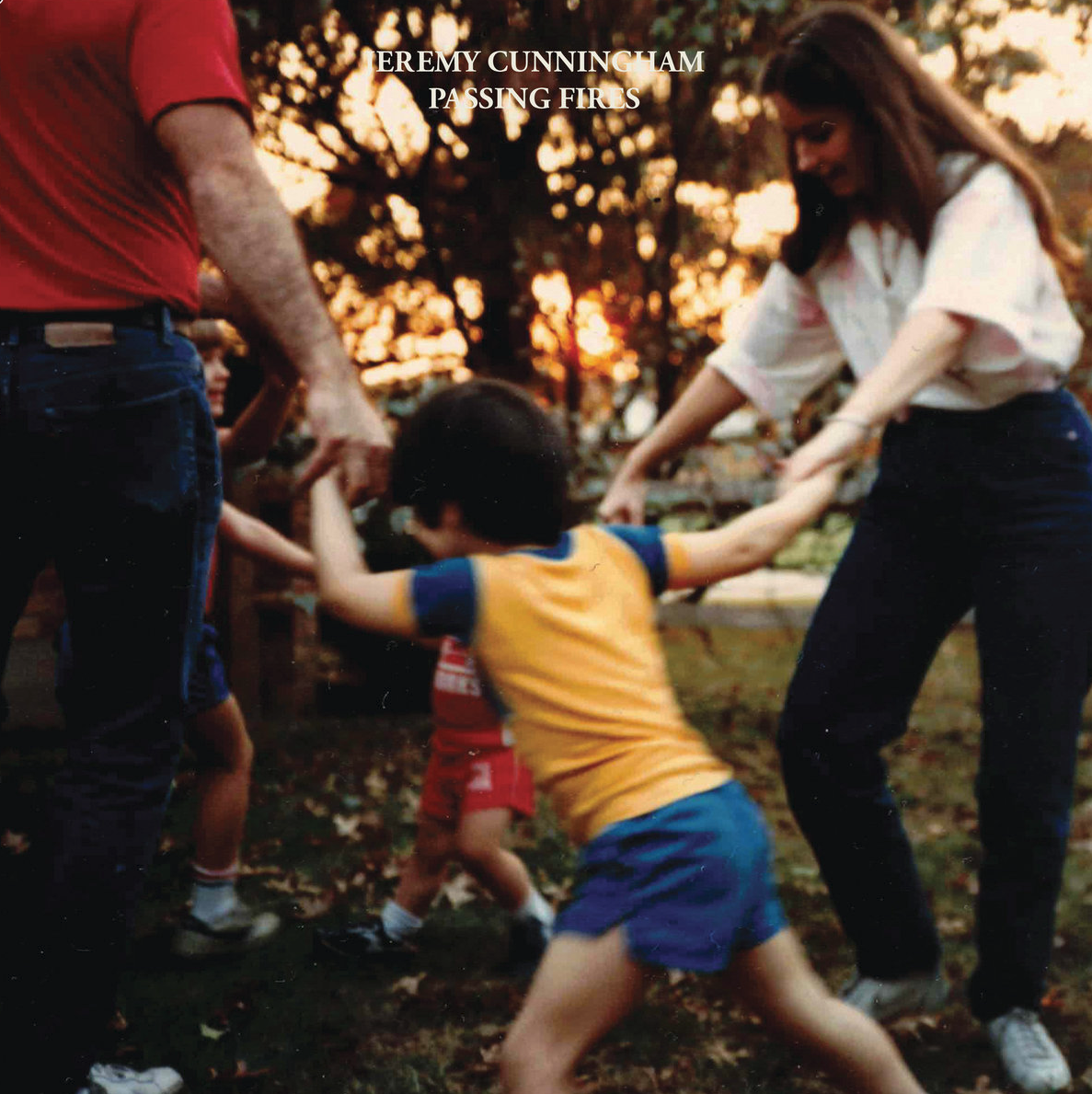 A group of people, including a child in a yellow and blue outfit, are holding hands and playing outside at sunset.