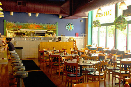 interior of Wishbone Restaurant on Washington in Chicago IL with wooden chairs and tables, a counter with stools, and large windows letting in natural light is shown.