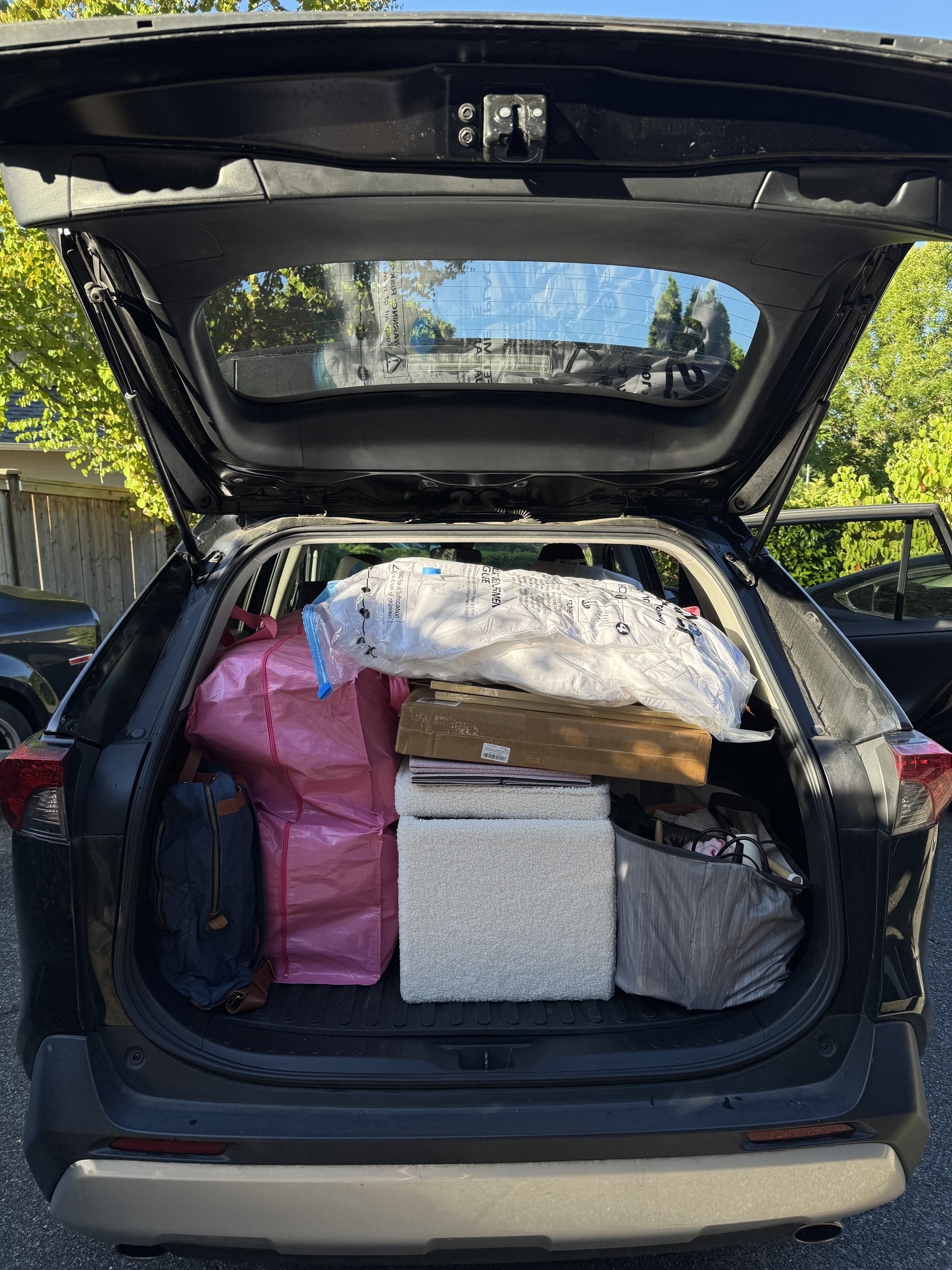 An open car trunk is filled with various items including a backpack, packages, and a cooler.