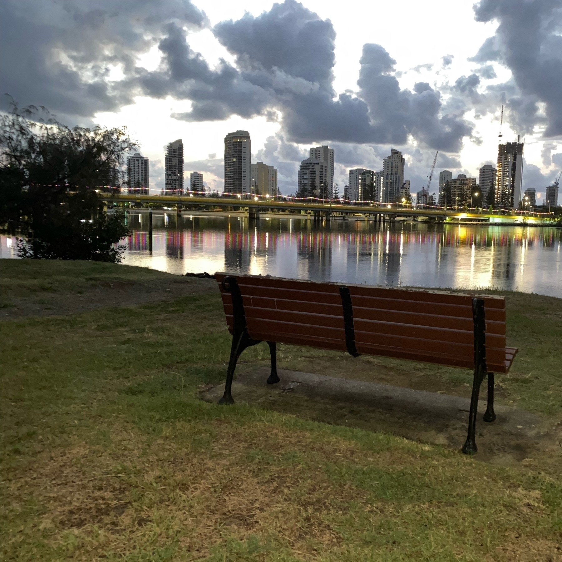 early morning photo of a park bench looking out over a river with nice cloud formations. 