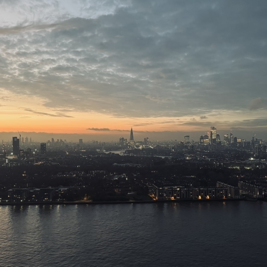 A picture of London's skyline, looking West, towards the Shard. The sun is setting, and in the foreground we can see the river Thames as it flows past Canary Wharf.