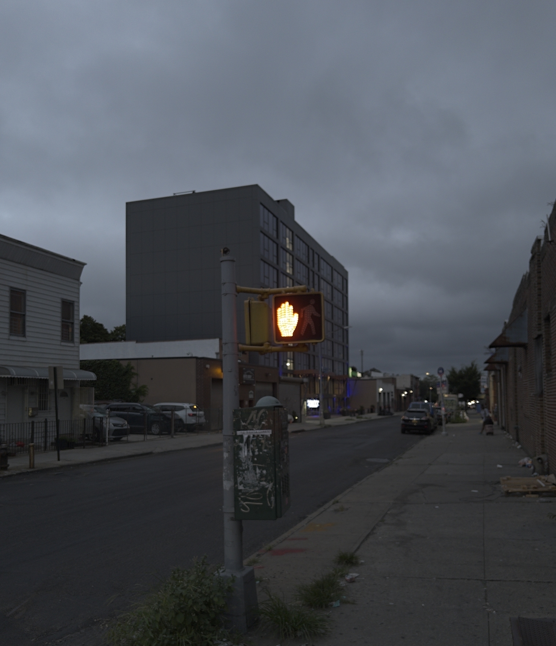 A desaturated city street. No one in frame. No cars moving. The walk sign is red, it’s luminescence glowing against the grey. &10;