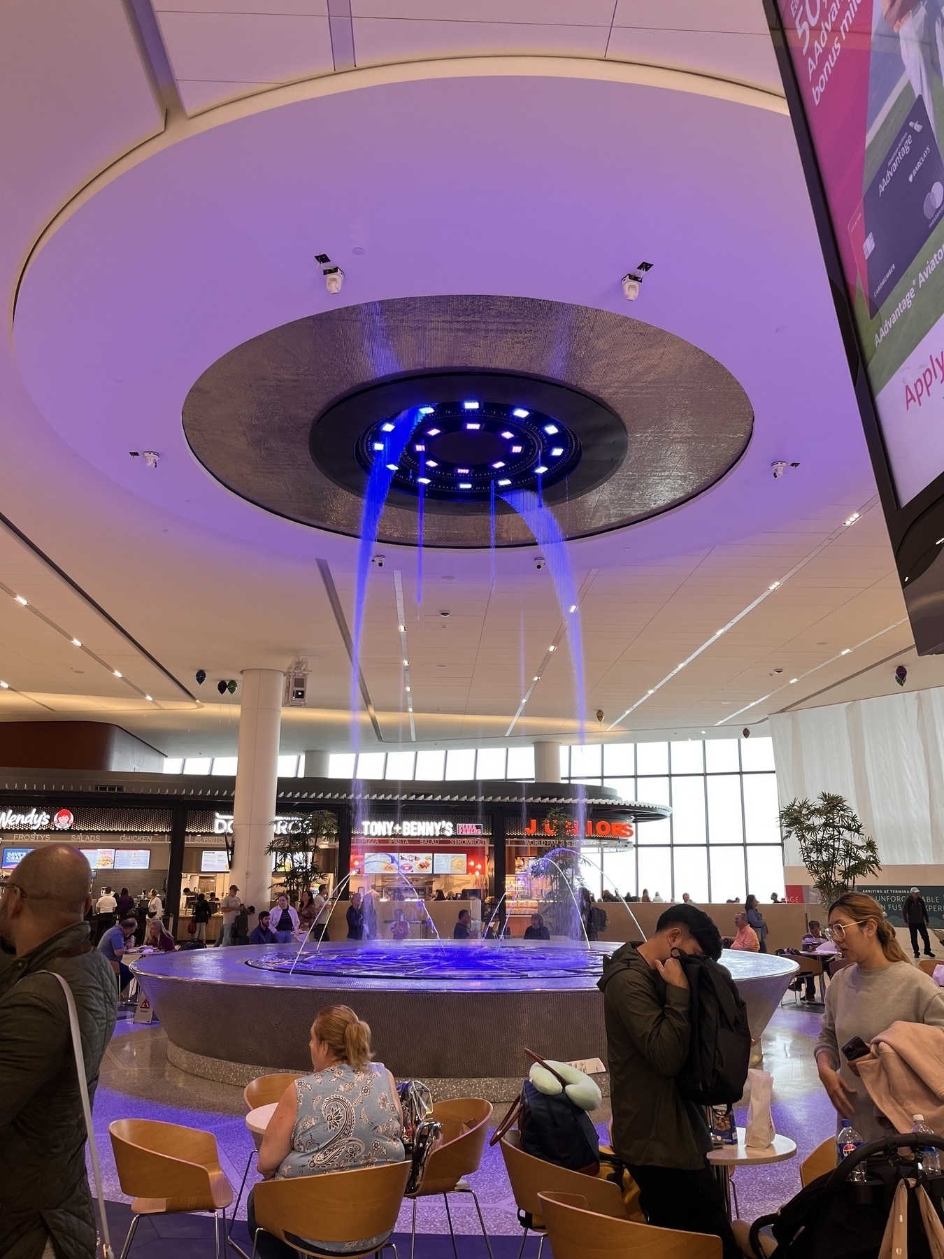 A swirling fountain with jets of water coming from the ceiling in fancy configurations and lighting in multiple colors. 