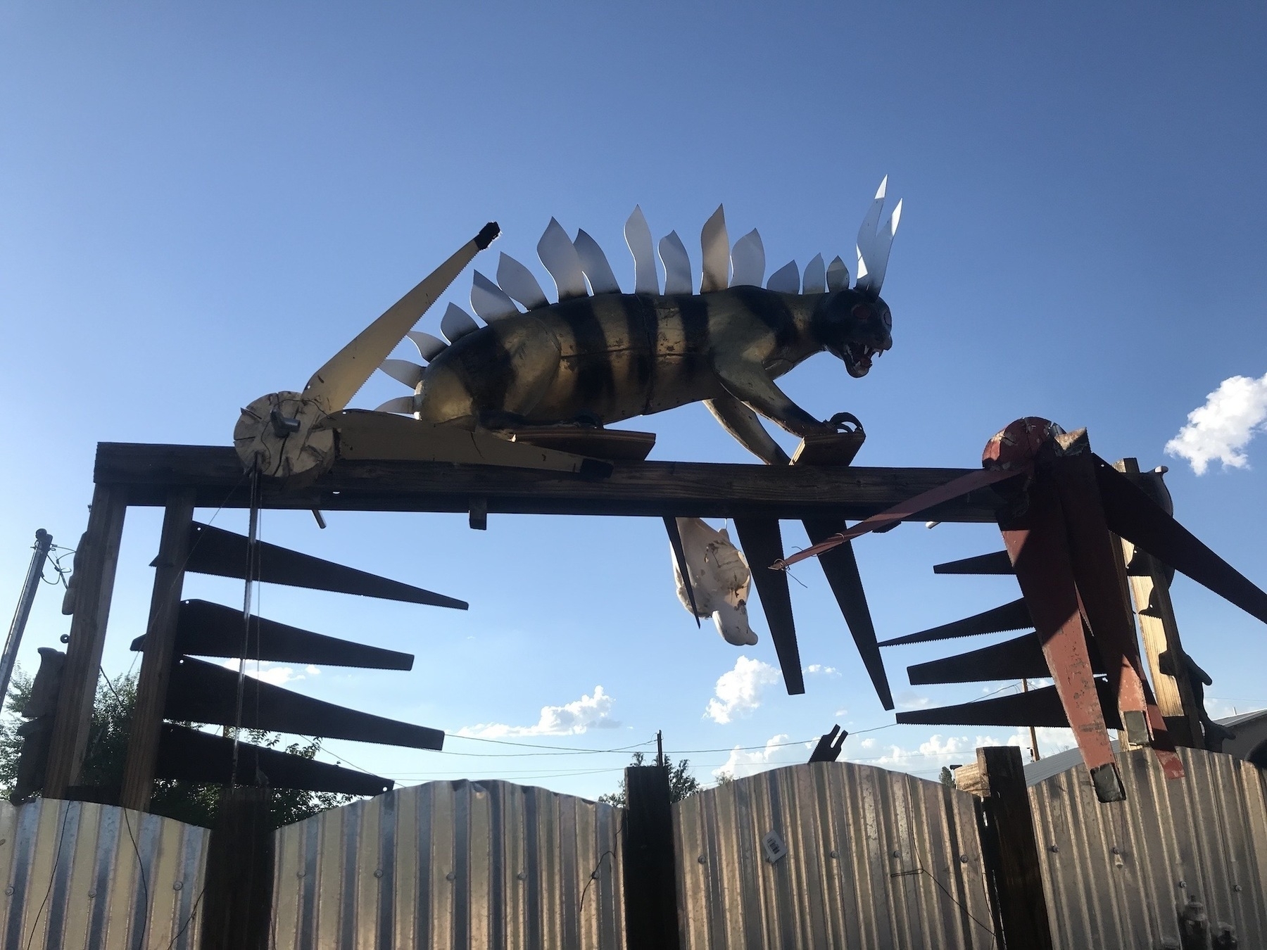 Low angle of a tin gate with an arch over it, and a metal scupture of some sort of metalic cat sitting on top