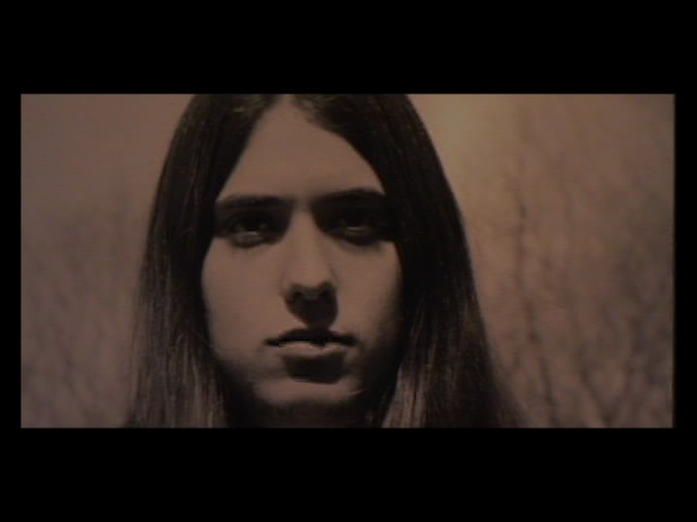 Close-up of a person with long straight dark hair and a neutral expression. The person is directly facing the camera and the image has a monochromatic sepia tone, giving it an aged appearance reminiscent of early photography.