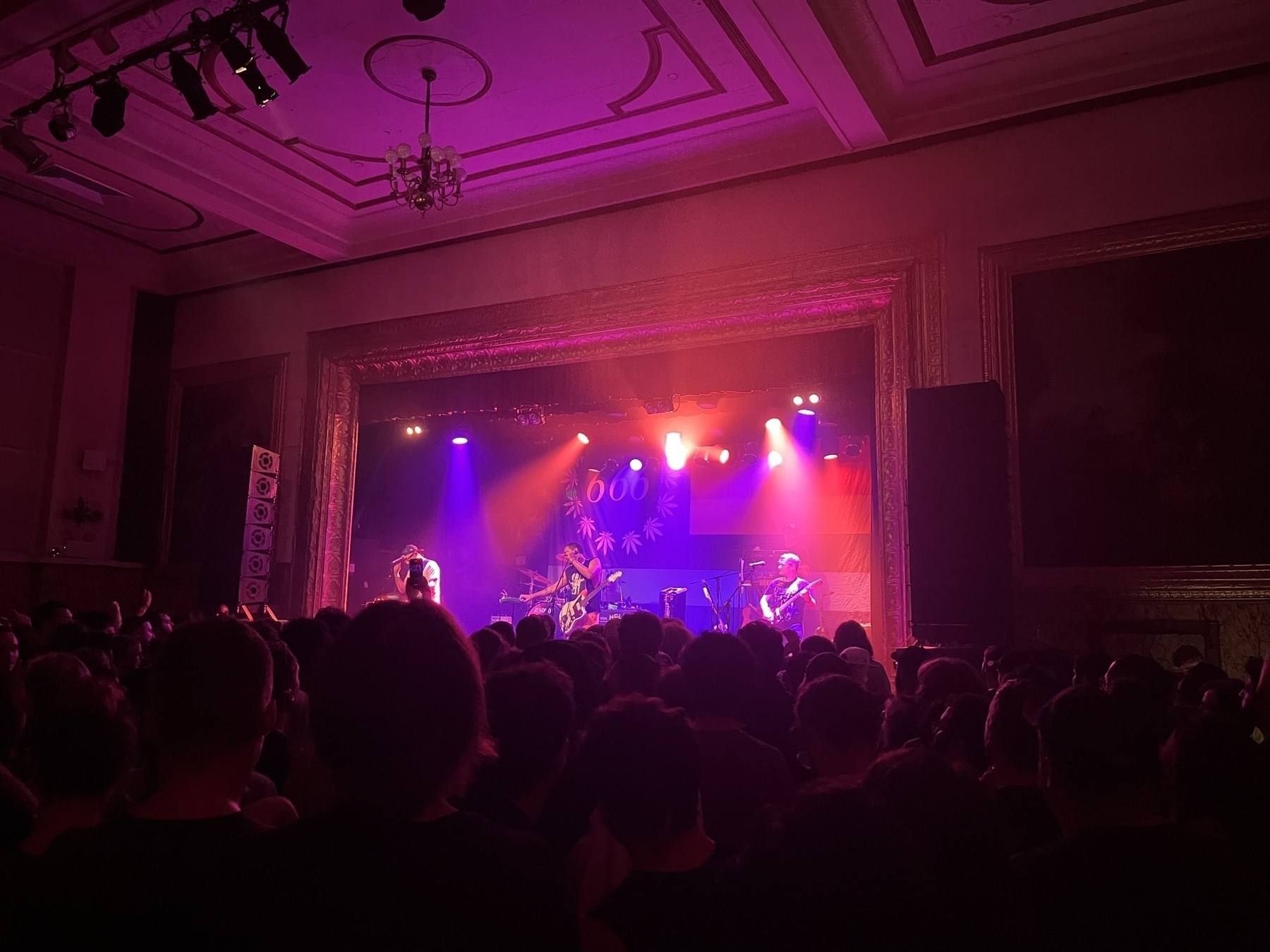 A purple lit stage with a crowd in high shadow in front. An older punk band plays on stage. 