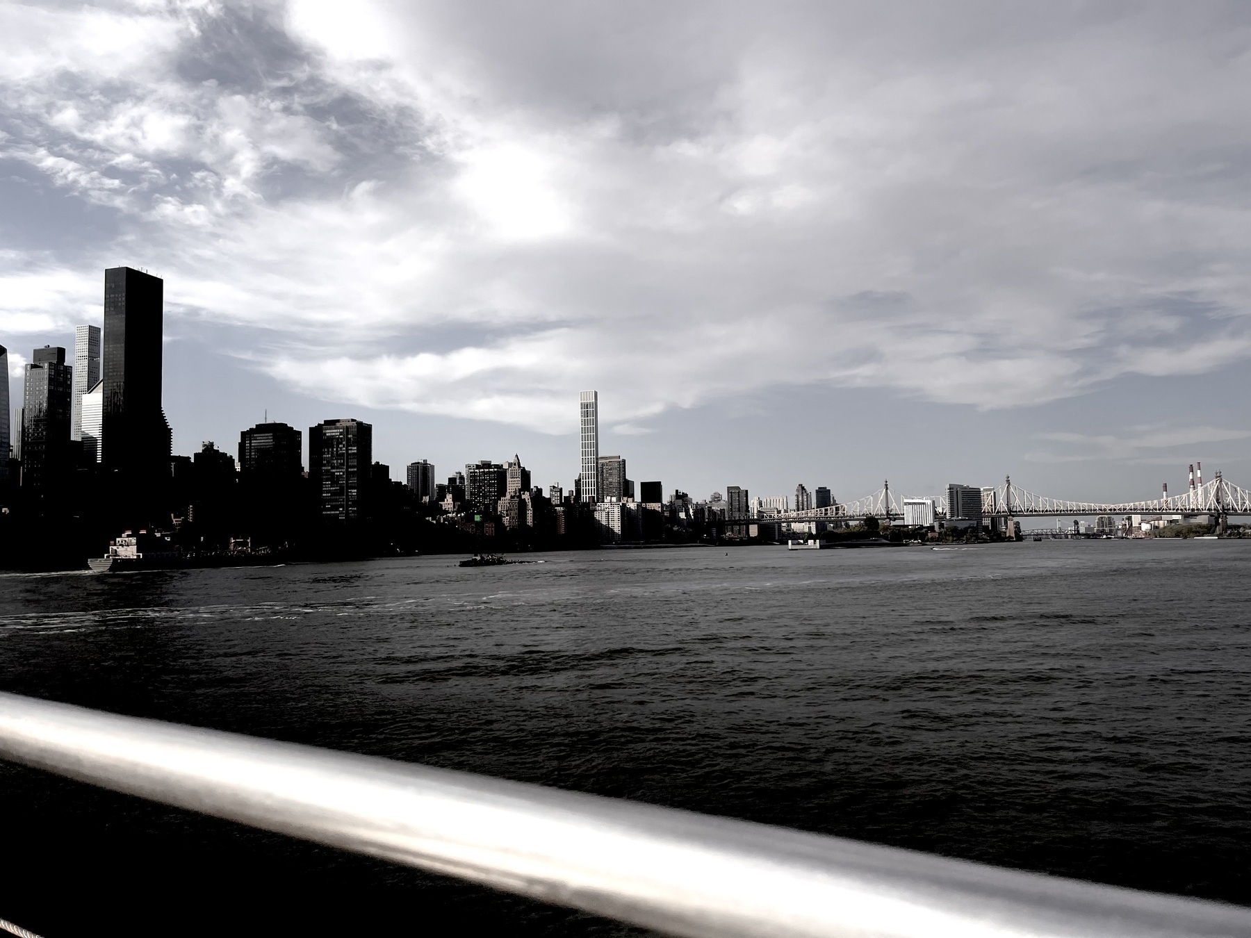 The water spread out with Manhattan in the background. The triboro bridge is in the far distance. Everything has a washed out, greyish quality.  