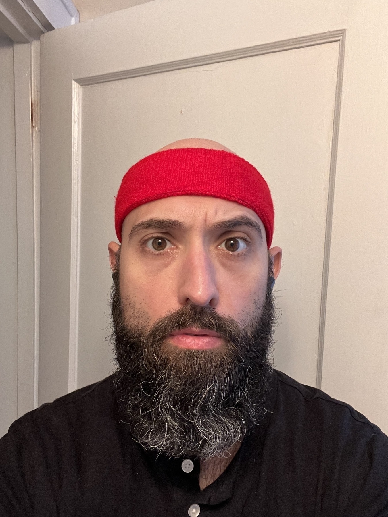 A photo of me, a white guy with a bald head long beard, wearing a bright red headband and a worried expression. 