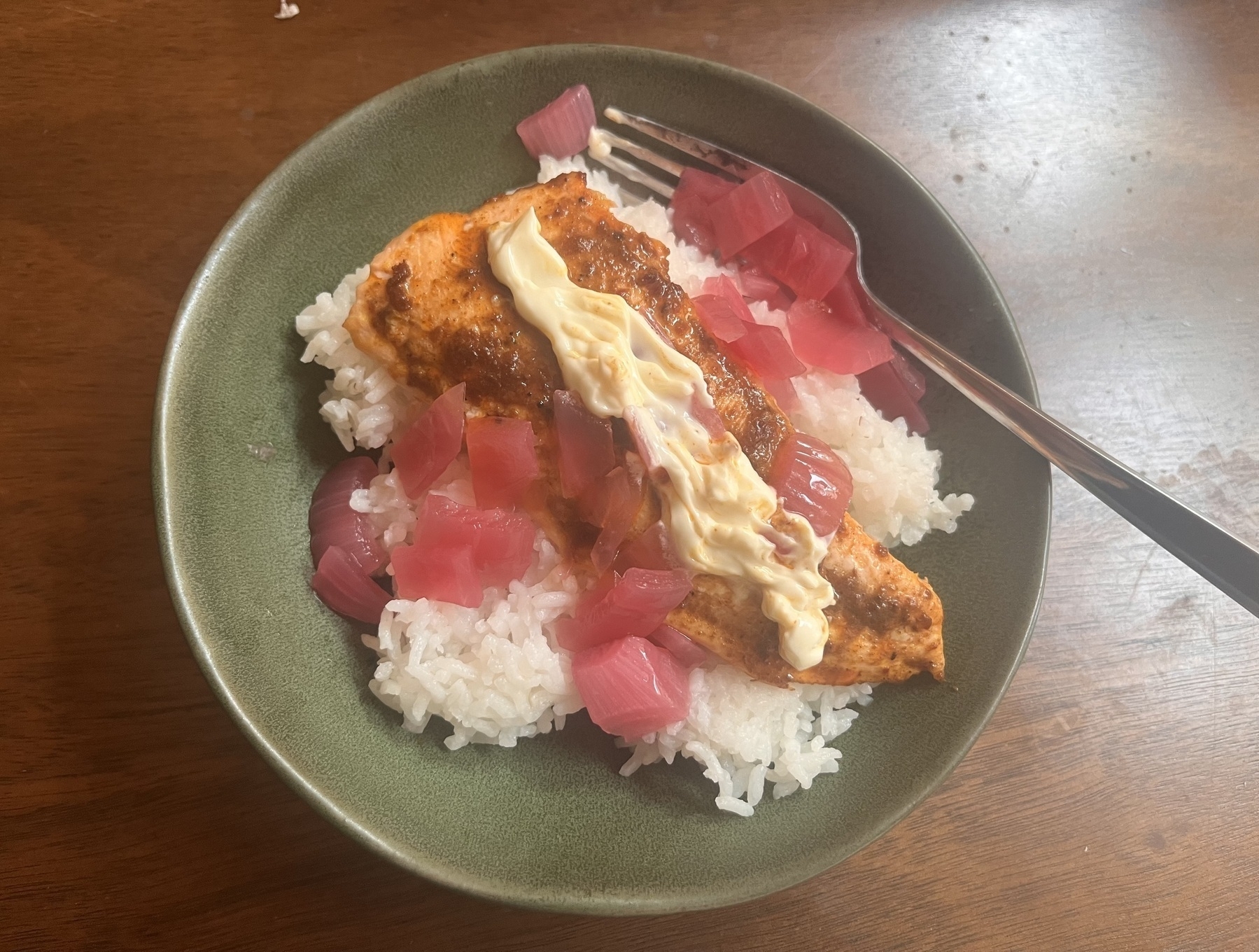 A bowel of white rice with a half cut of curried salmon on top. There’s some pickled red onions scattered around, along with a ribbed snake of mayo. 