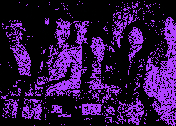 Grainy black and purple photo of a bunch of white and asian German rock musicians standing in a row behind some recording equipment. Everyone has 70s long hair.