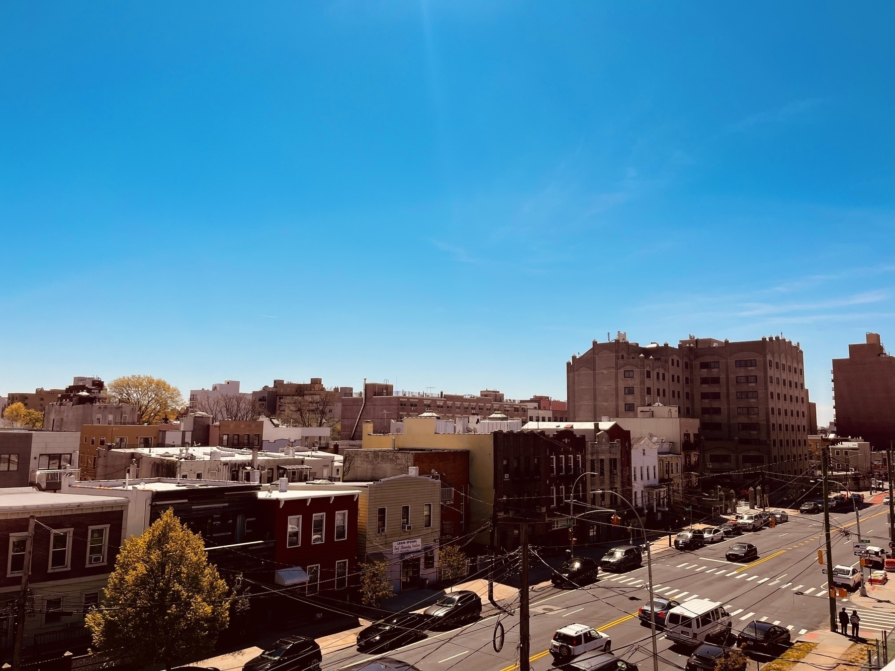 Residential brick two and three story buildings with a wide street running h through the foreground. Taken from a high angle. A bright blue sky takes up most of the top of the image. 