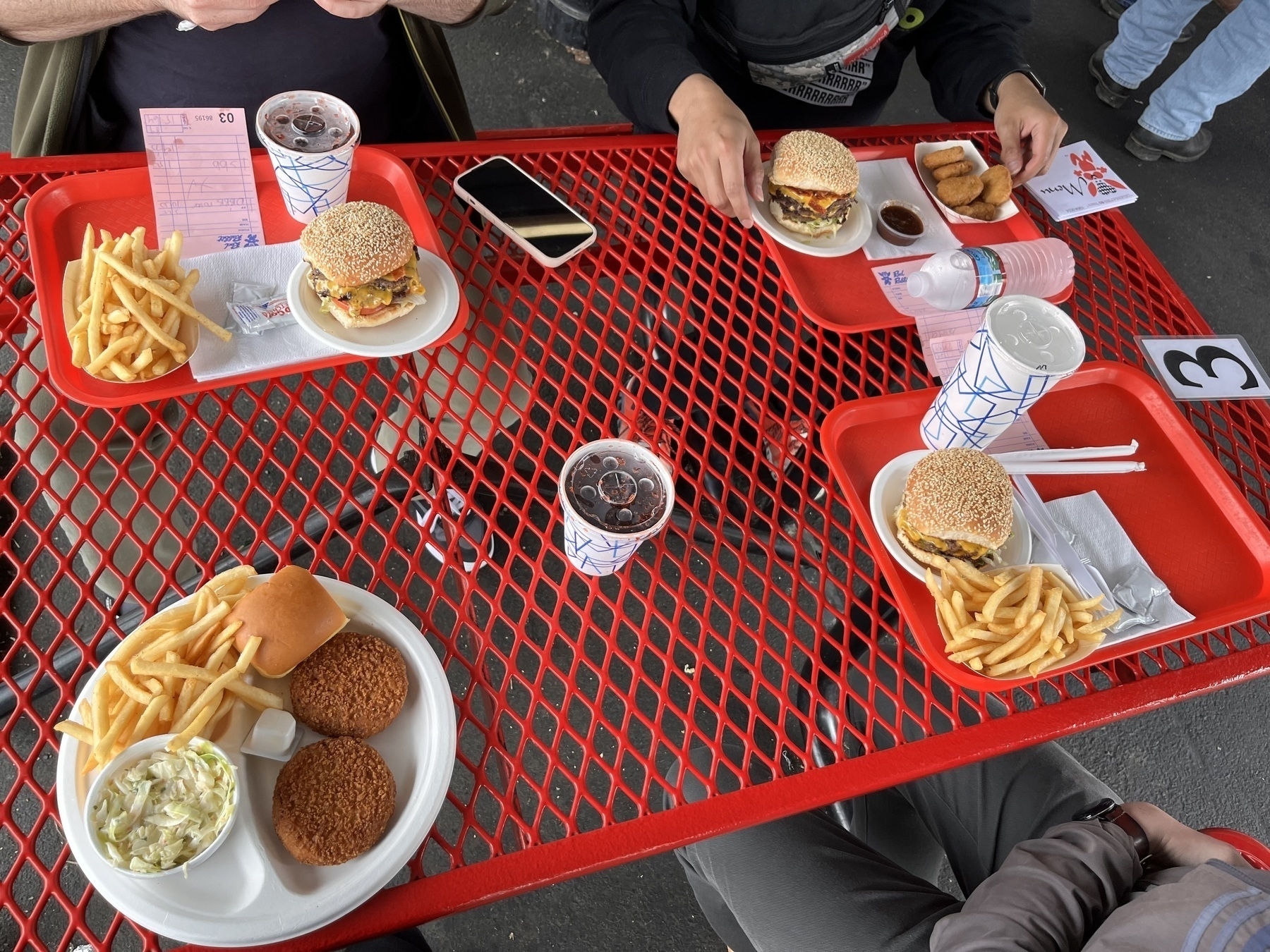 Fast food on a red latticed table. Burgers, fries, birch soda, and a plate of crab cakes. 