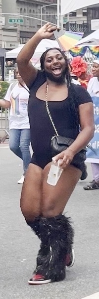 A black trans woman waving joyfully with mouth open and posing coyly.