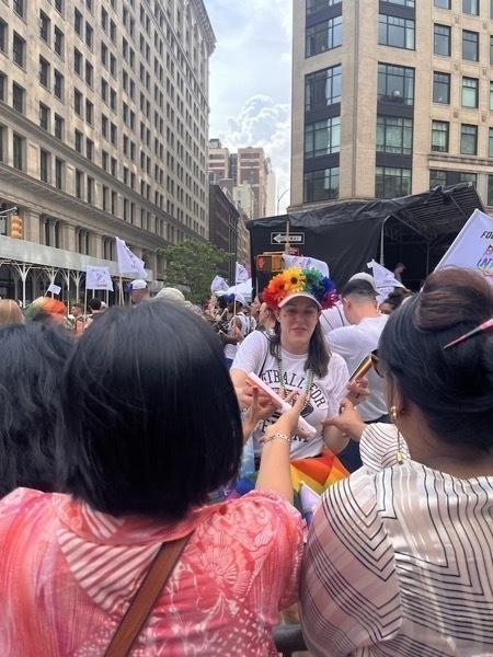 A woman wearing a rainbow flower hat hands out merch to eager onlookers.