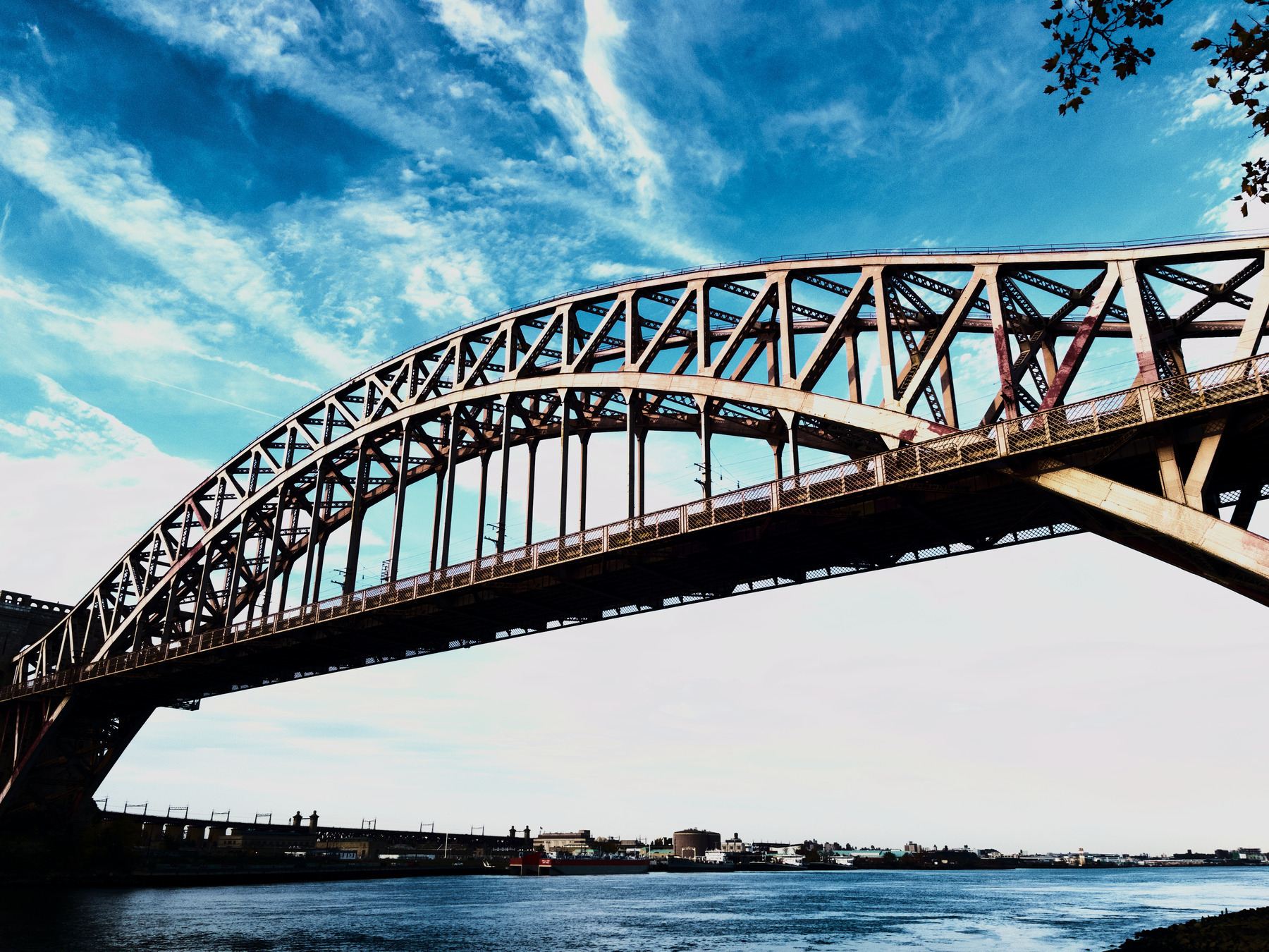 Auto-generated description: A steel arch bridge spans across a body of water under a partly cloudy sky.