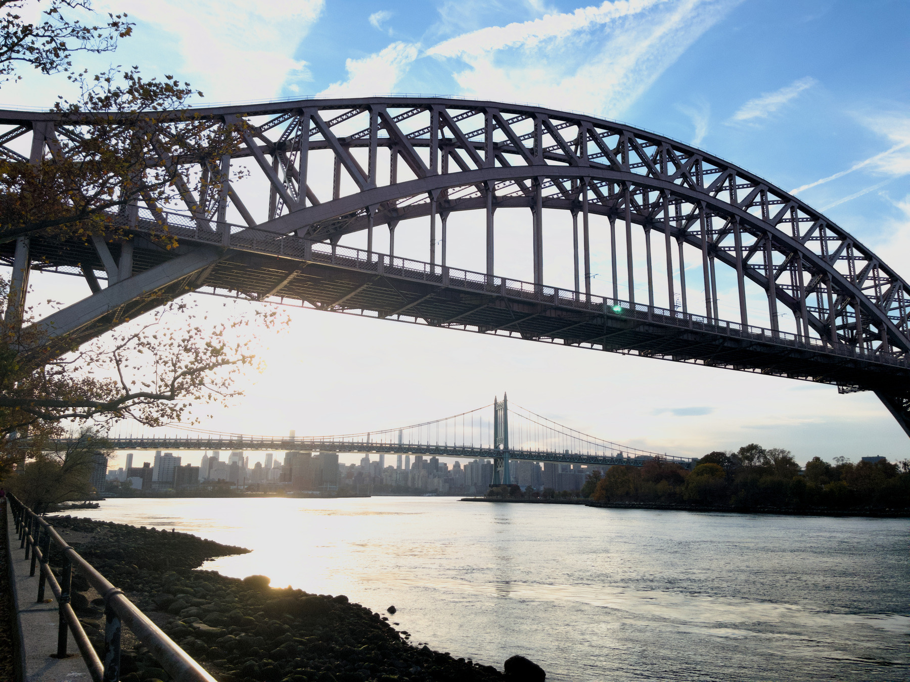 Auto-generated description: A large arch bridge spans over a calm body of water with a second bridge and a cityscape visible in the distance.