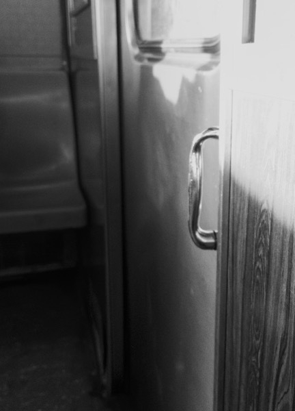 Black and white photo of the inside of the N NYC subway train, close up of the door handle between trains.