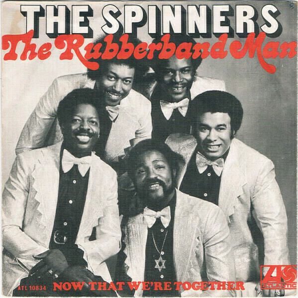 Auto-generated description: Five men in suits are smiling and posing together, with the text The Spinners and The Rubberband Man at the top.