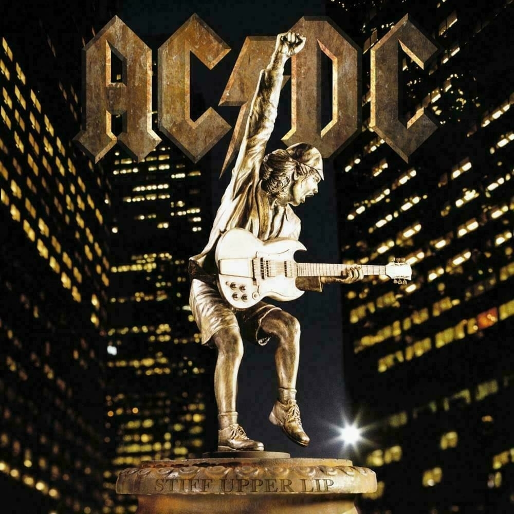 Auto-generated description: A gold statue of a guitarist, Angus Young, holding an electric guitar stands tall in front of a cityscape at night, with AC/DC written above.