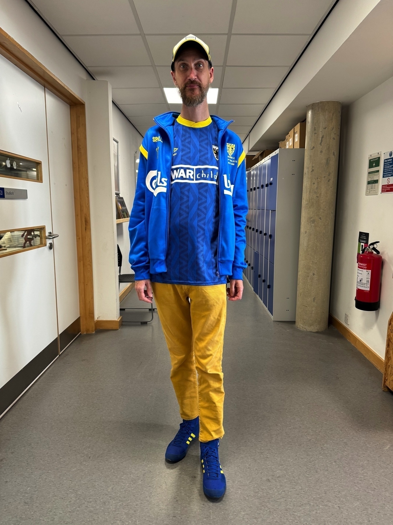 Photo of me (Adam Procter) in my football going outfit, blue and yellow trainers, yellow jeans, new warchild home yellow and blue top, replica 1988 walk out FA cup jacket, AFC Wimbledon baseball cap